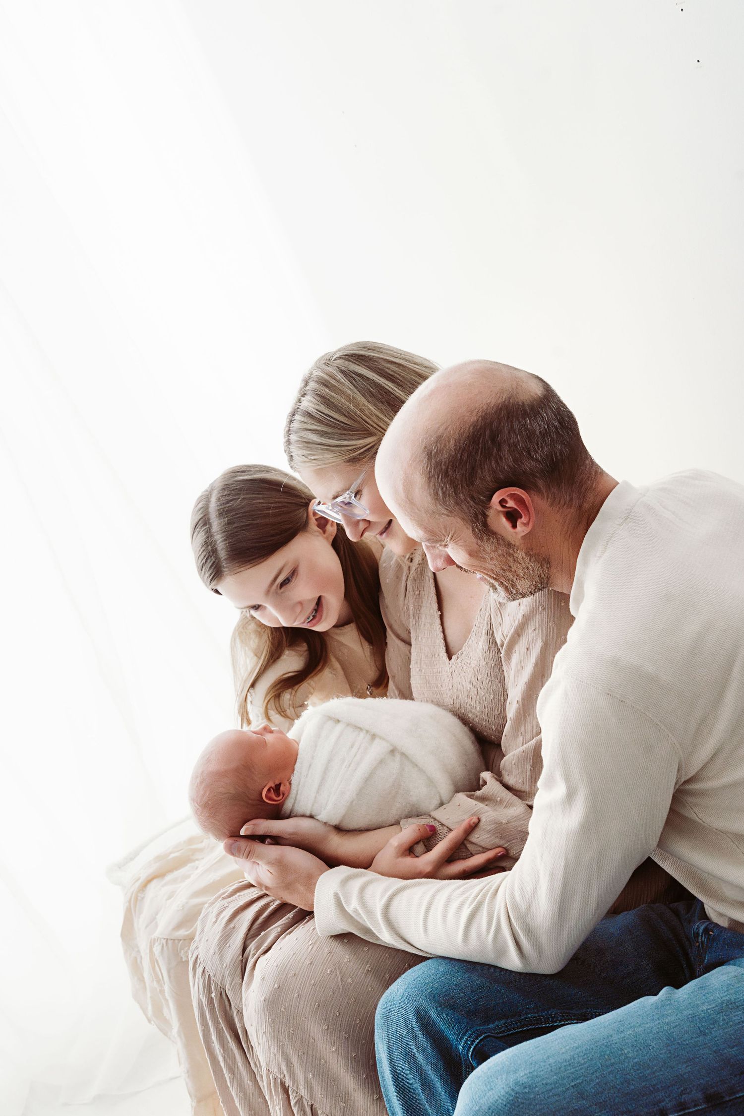 Happy family of three admiring their newborn baby wrapped in a white swaddle blanket.