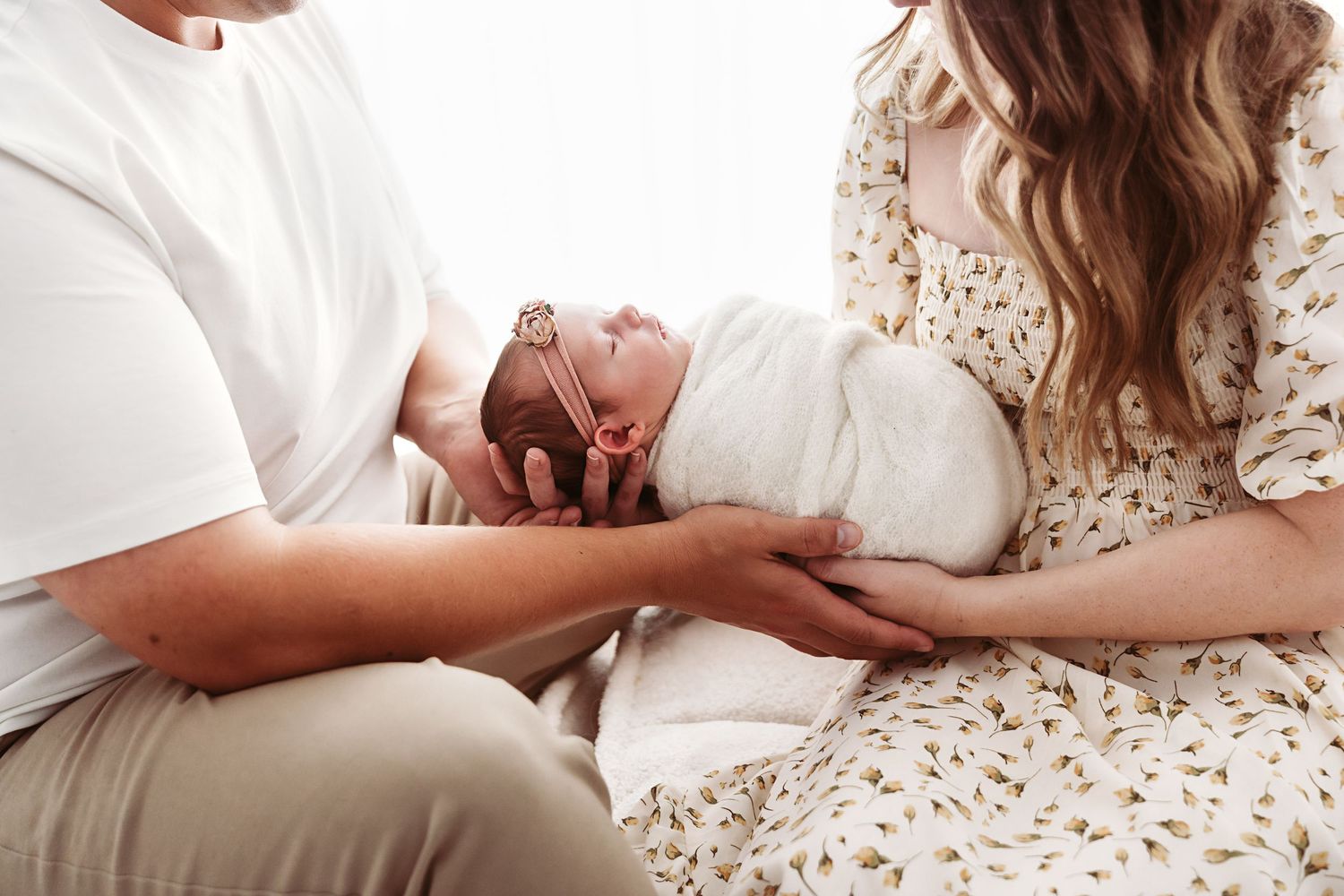 Close-up of parents cradling their swaddled newborn baby together in a tender, intimate moment.