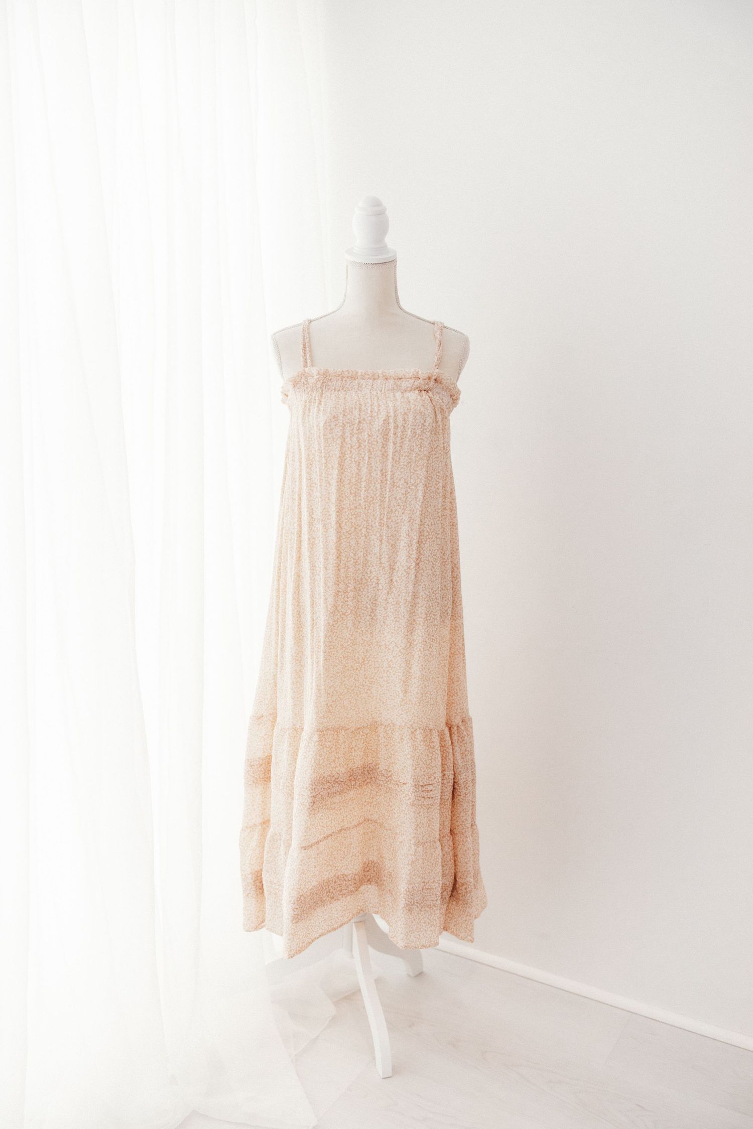 Beige spaghetti strap tiered maxi dress with fringe trim on white mannequin.