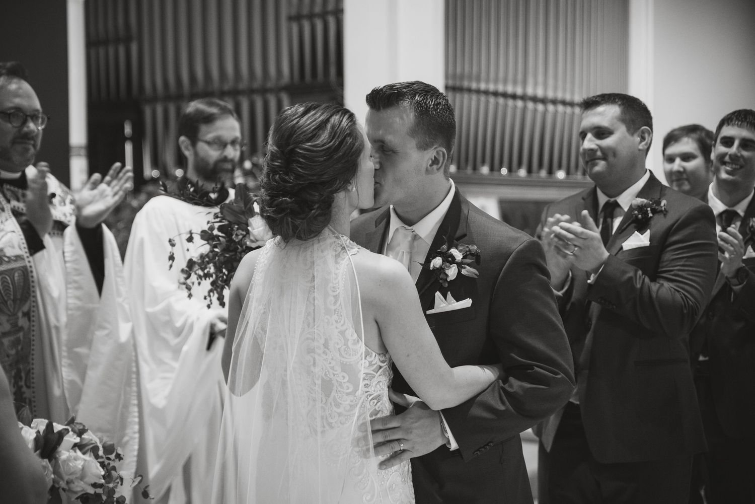 Bride and groom sharing their first kiss at the altar in a black and white photo.