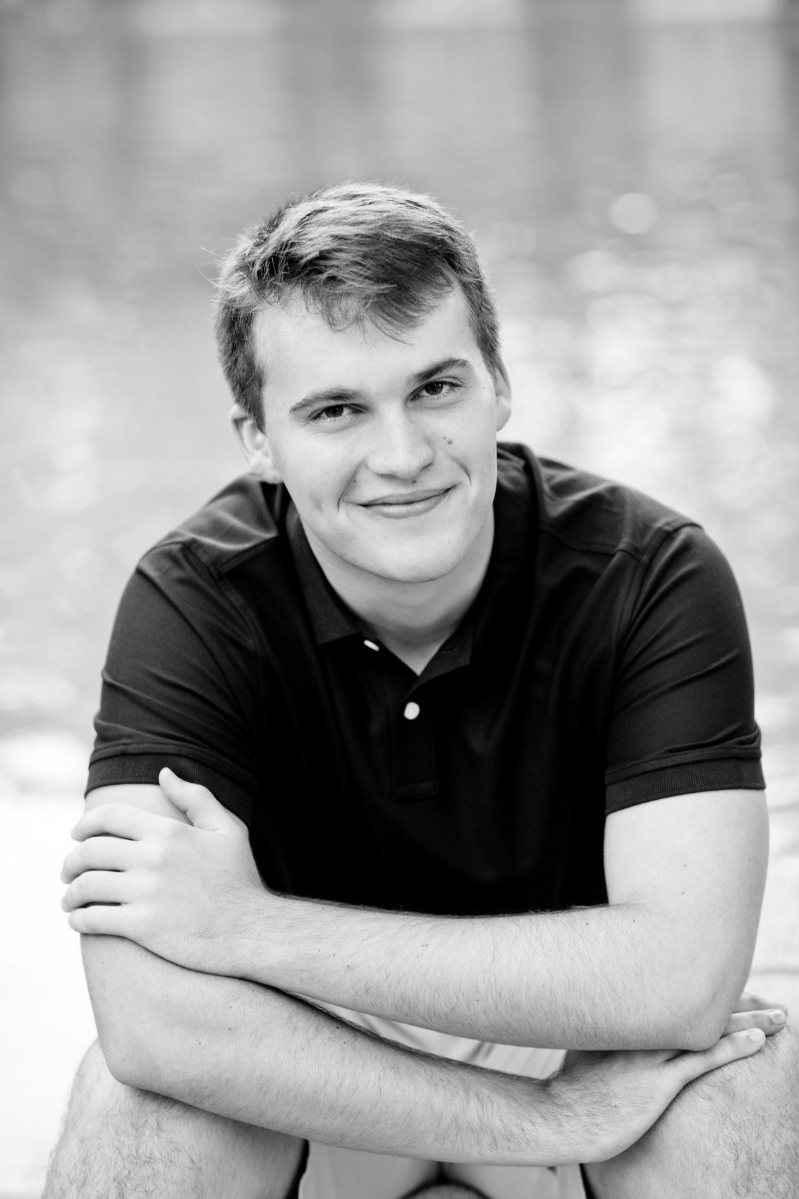 Black and white portrait of a smiling young man in a dark polo shirt with arms crossed.