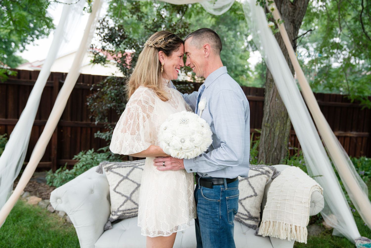 Couple sharing a romantic moment at an outdoor backyard wedding ceremony with white draping and couch.