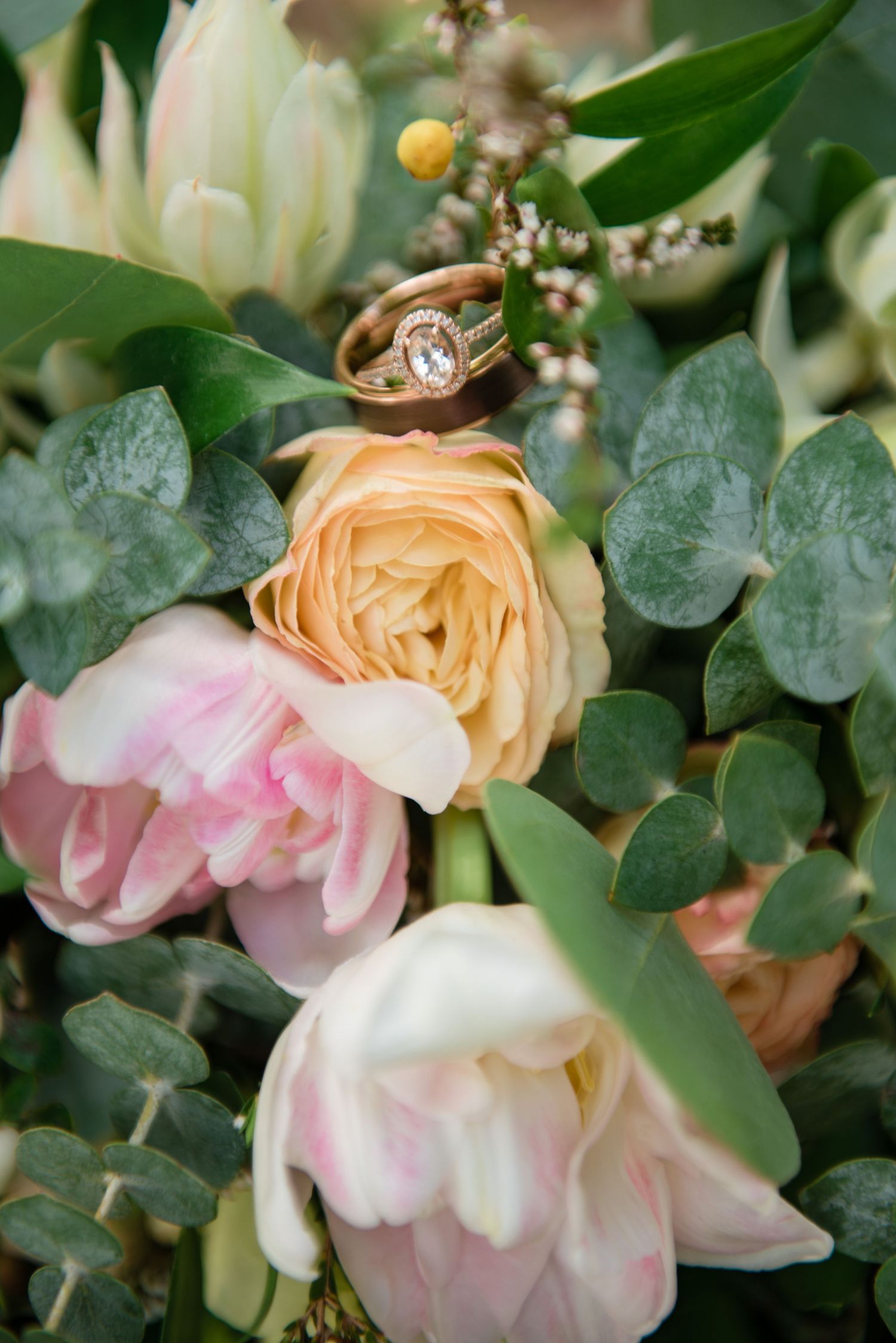 Rose gold oval engagement ring resting on peach and pink roses in bridal bouquet.
