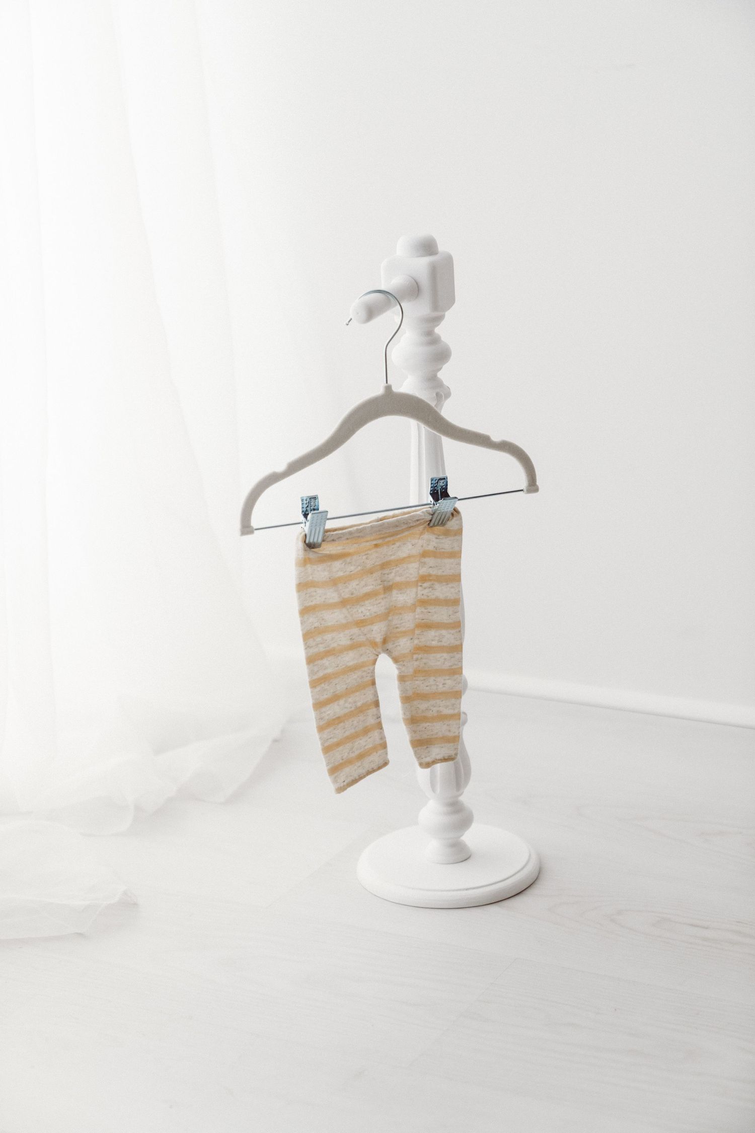 Beige and white striped baby leggings clipped to a velvet hanger on a white decorative stand.