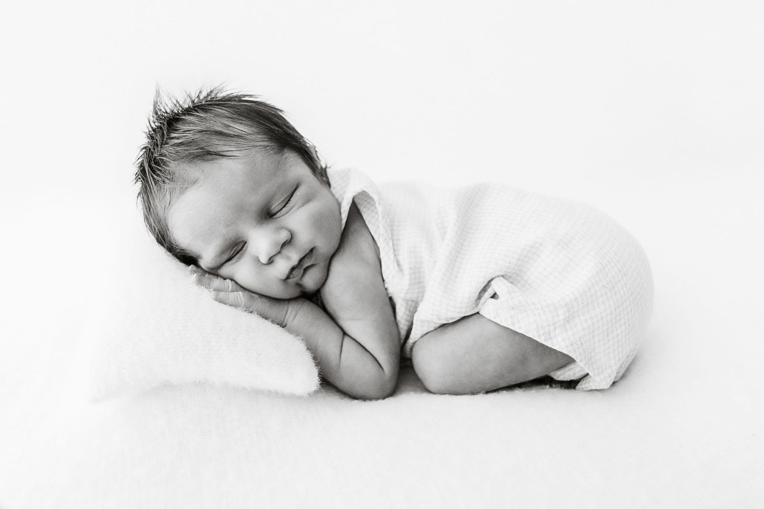 Black and white portrait of sleeping newborn baby posed on white pillow.