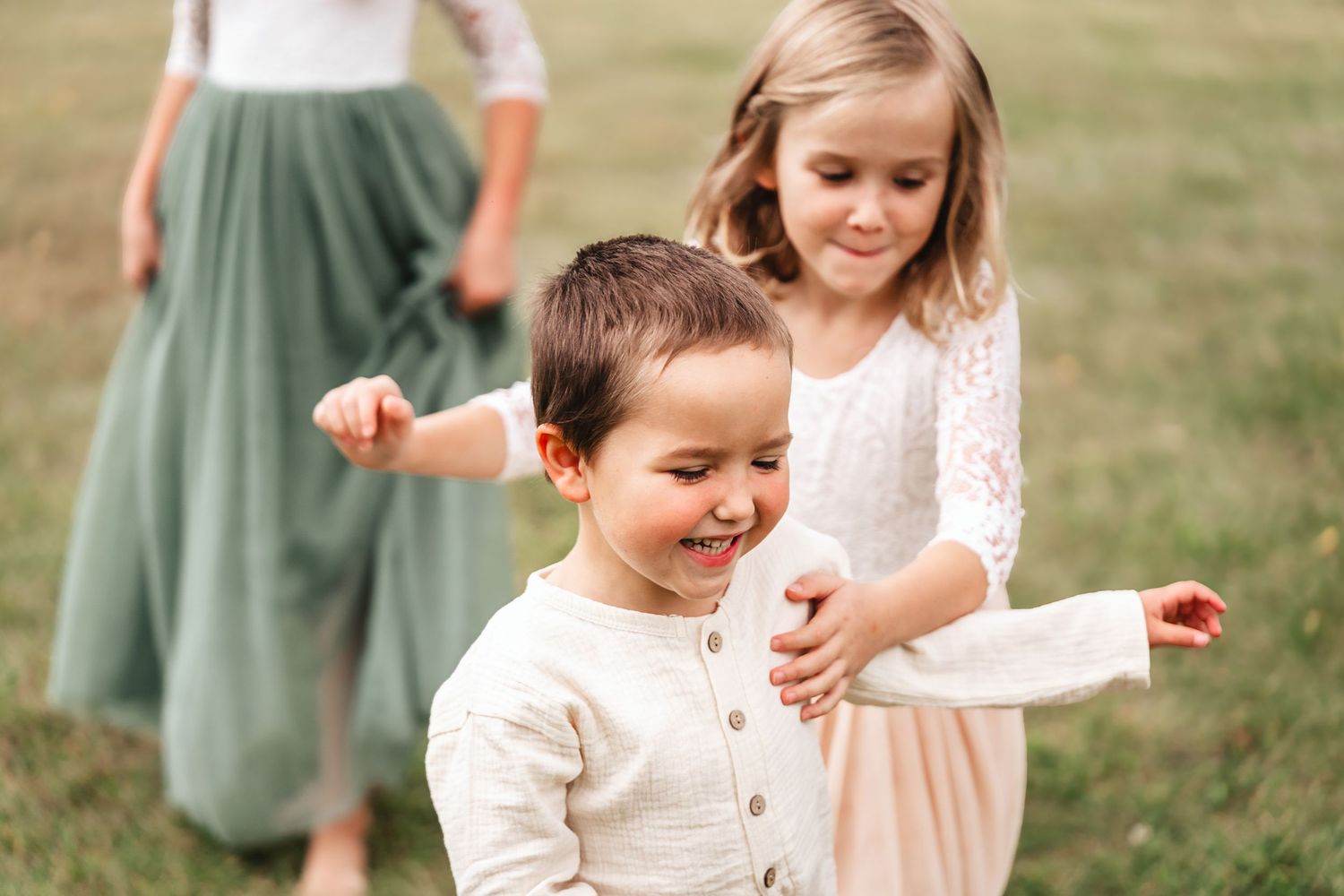 Two young children laugh and play together in an open grassy field.