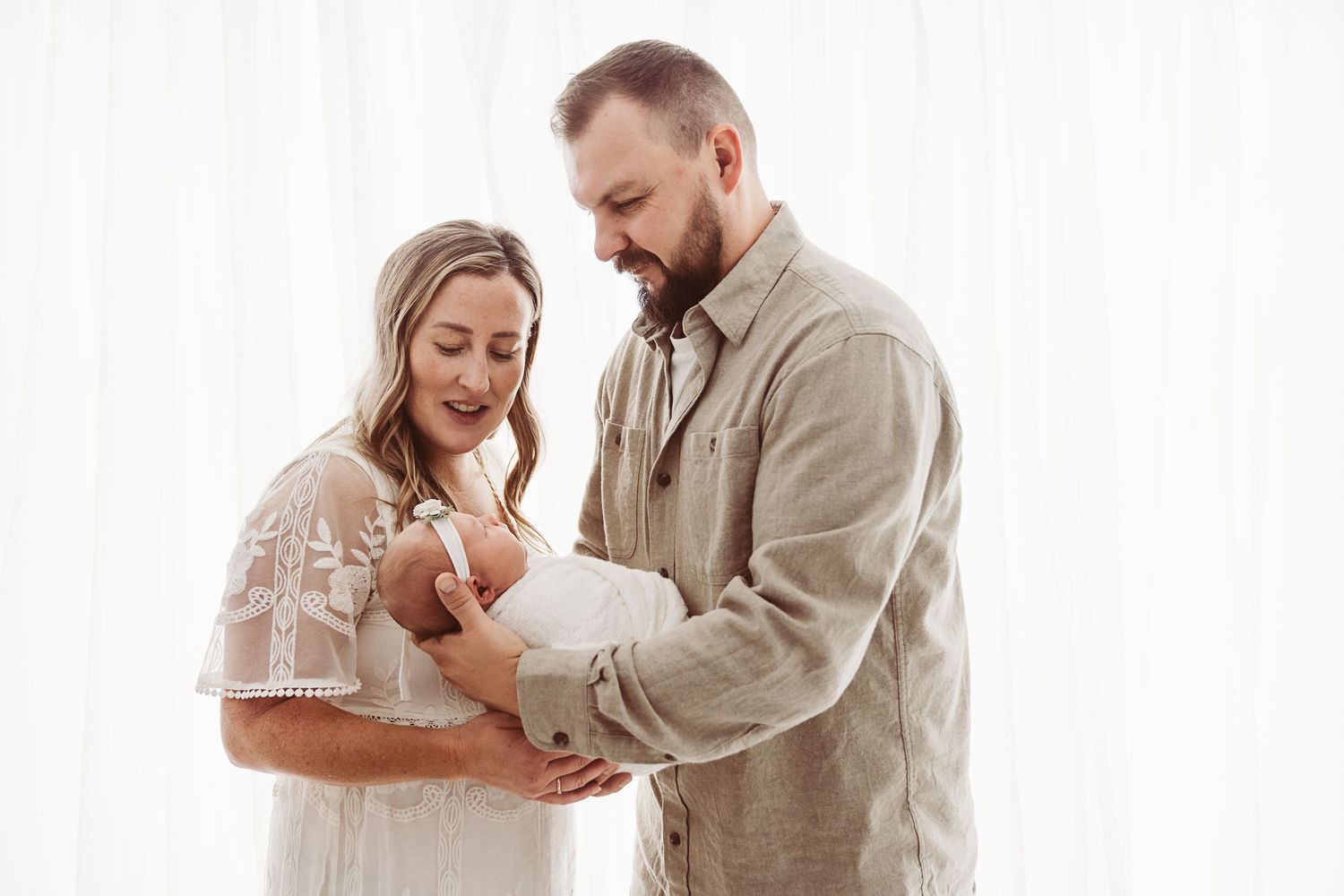 Happy parents smiling at their newborn baby during a professional newborn photography session.