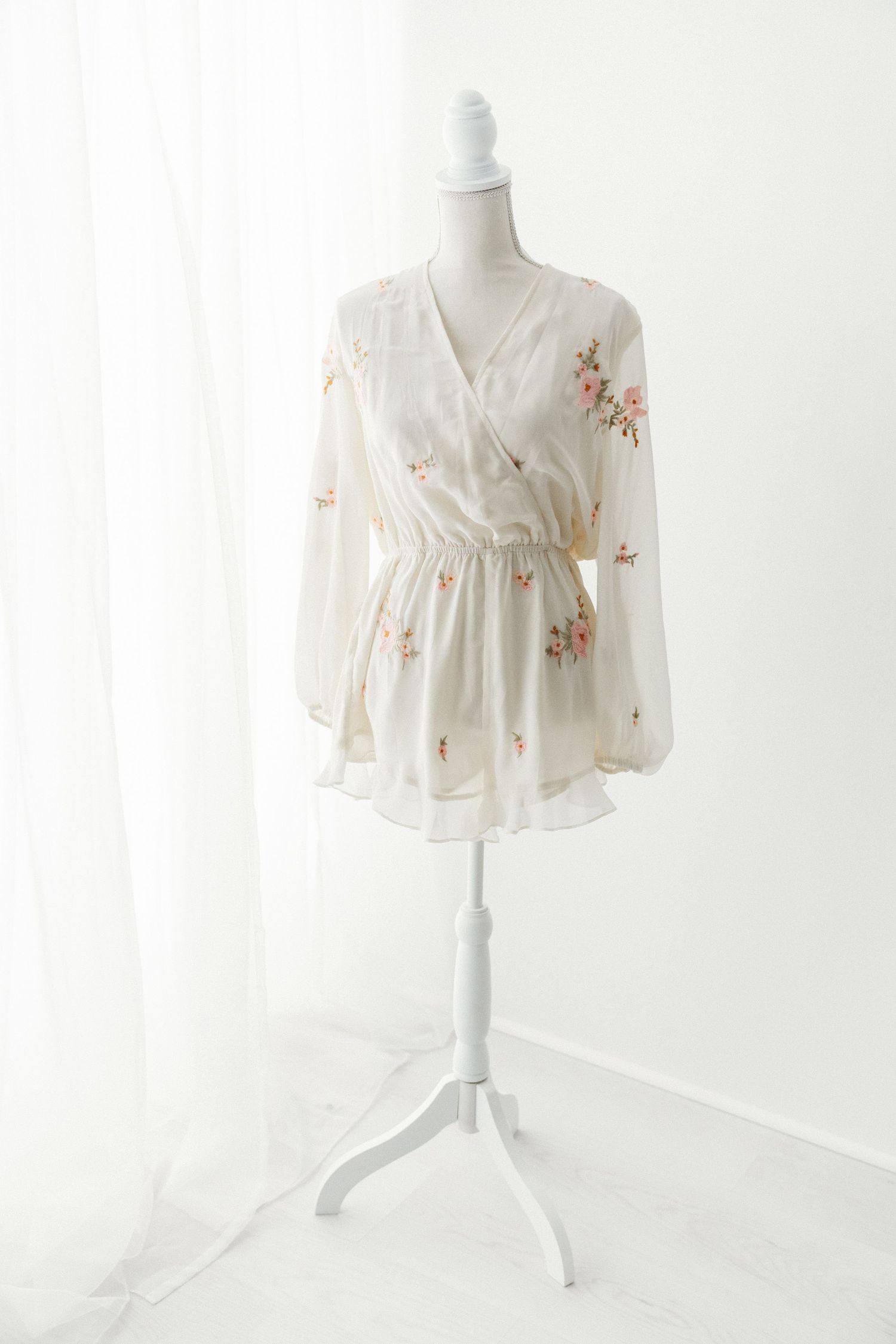White floral embroidered wrap blouse with long sleeves on mannequin.