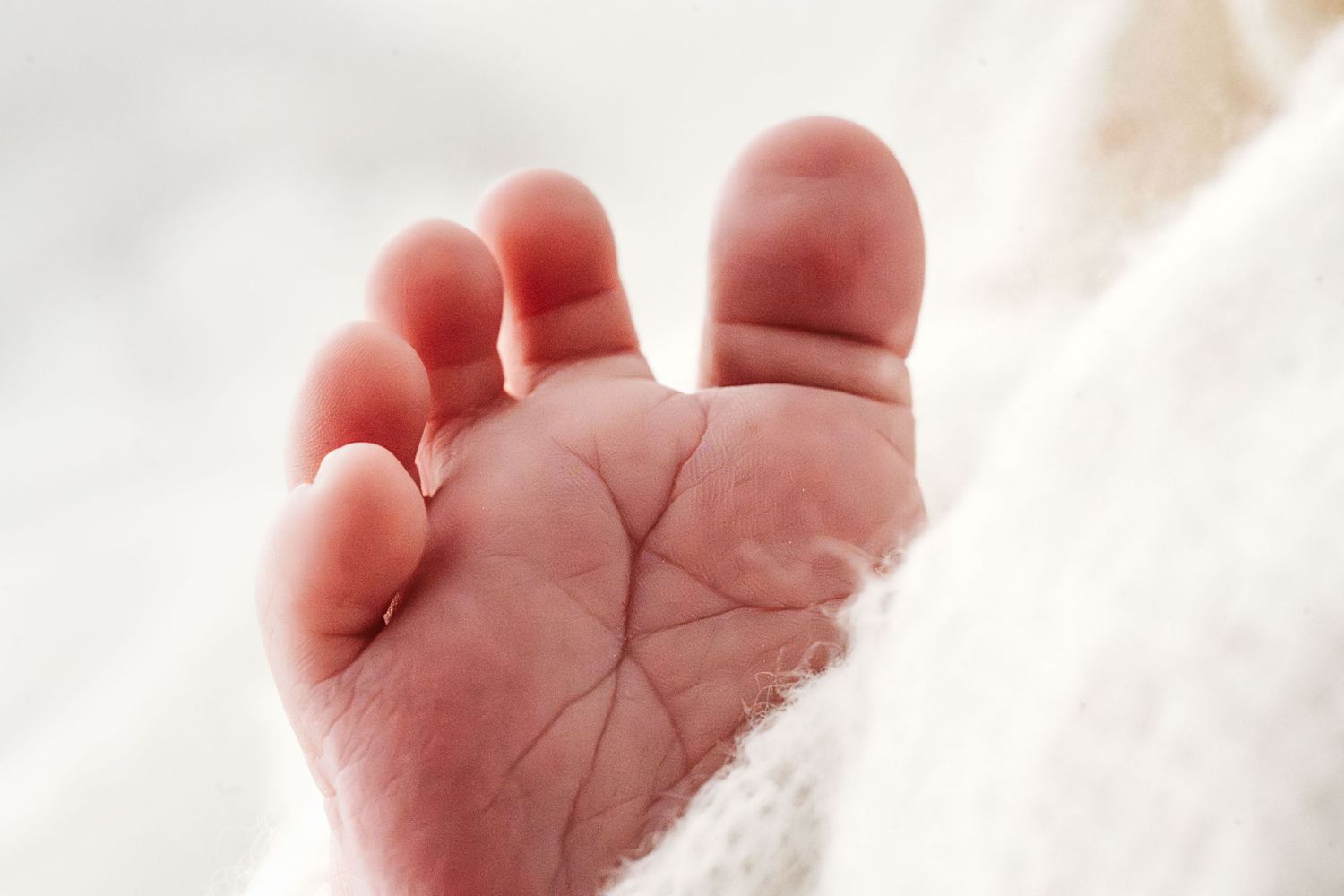 Extreme close-up of soft newborn baby foot sole with tiny toes on white blanket.