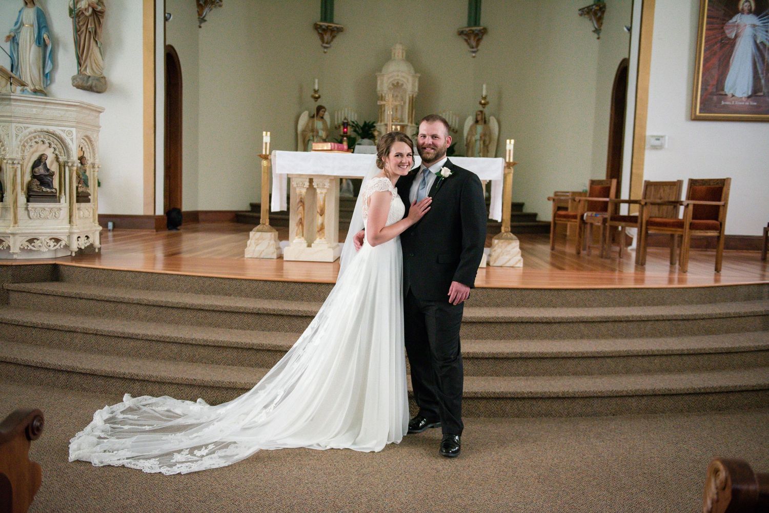 Bride and groom posing elegantly inside a church with long cathedral train and ornate altar backdrop.