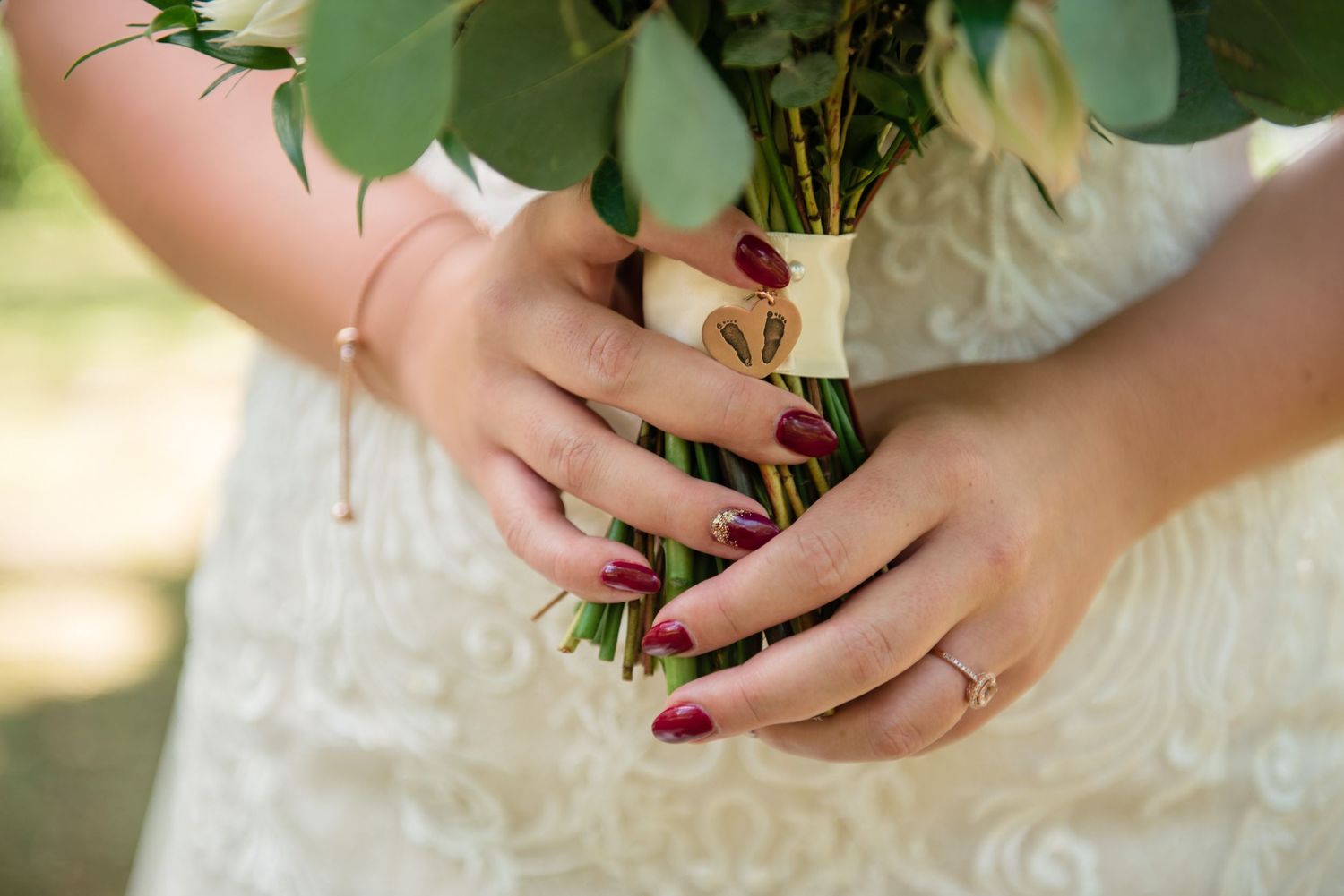 Bride holds eucalyptus bouquet with burgundy nails and diamond engagement ring visible.
