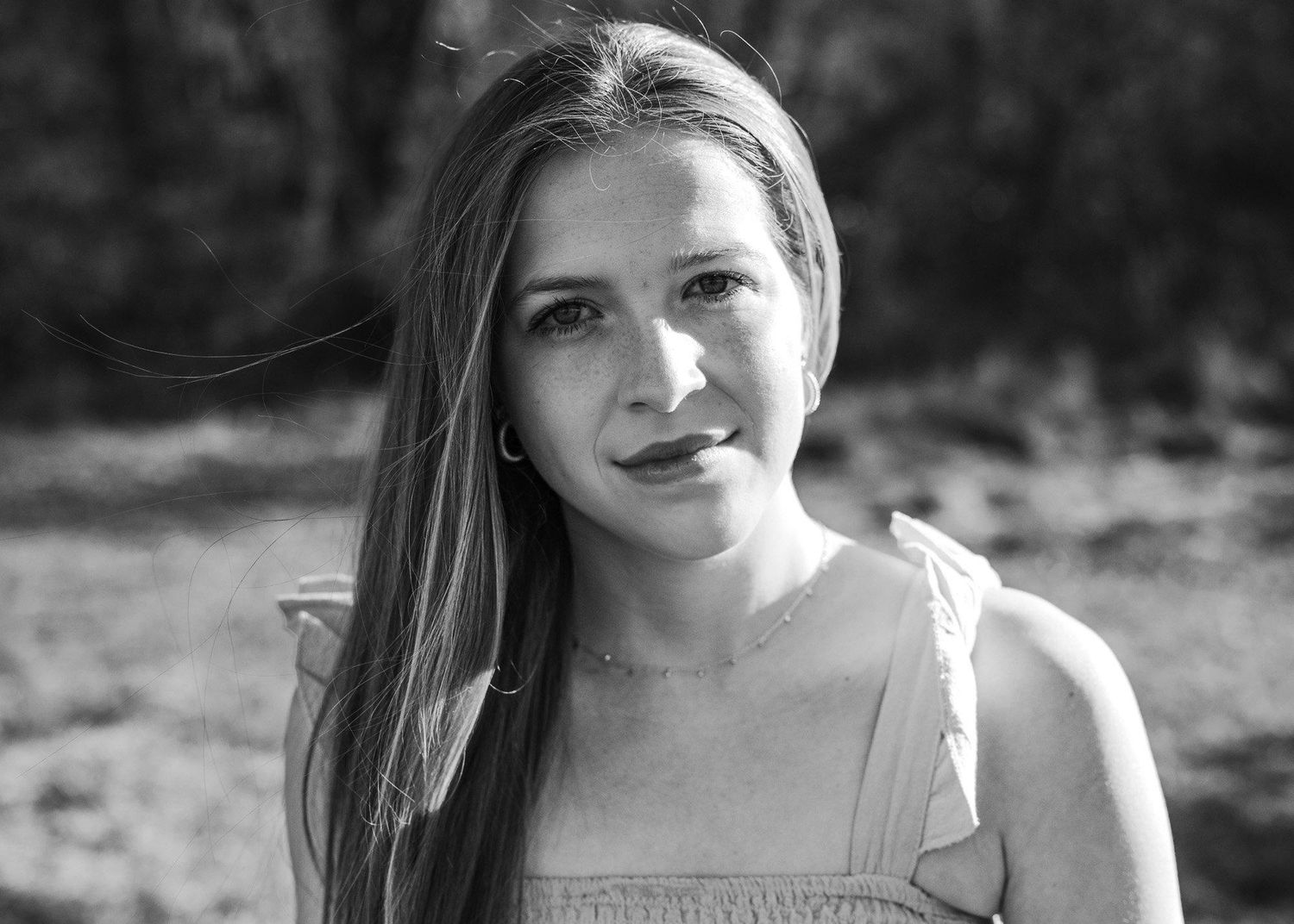 Black and white portrait of a young woman with long hair smiling softly outdoors.