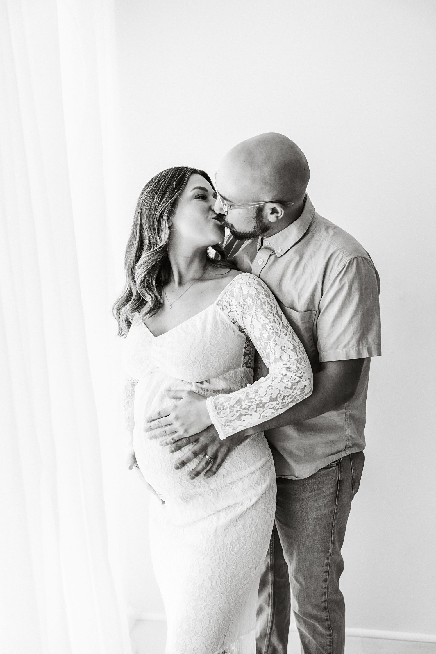 Black and white maternity photo of couple kissing while tenderly holding pregnant belly.