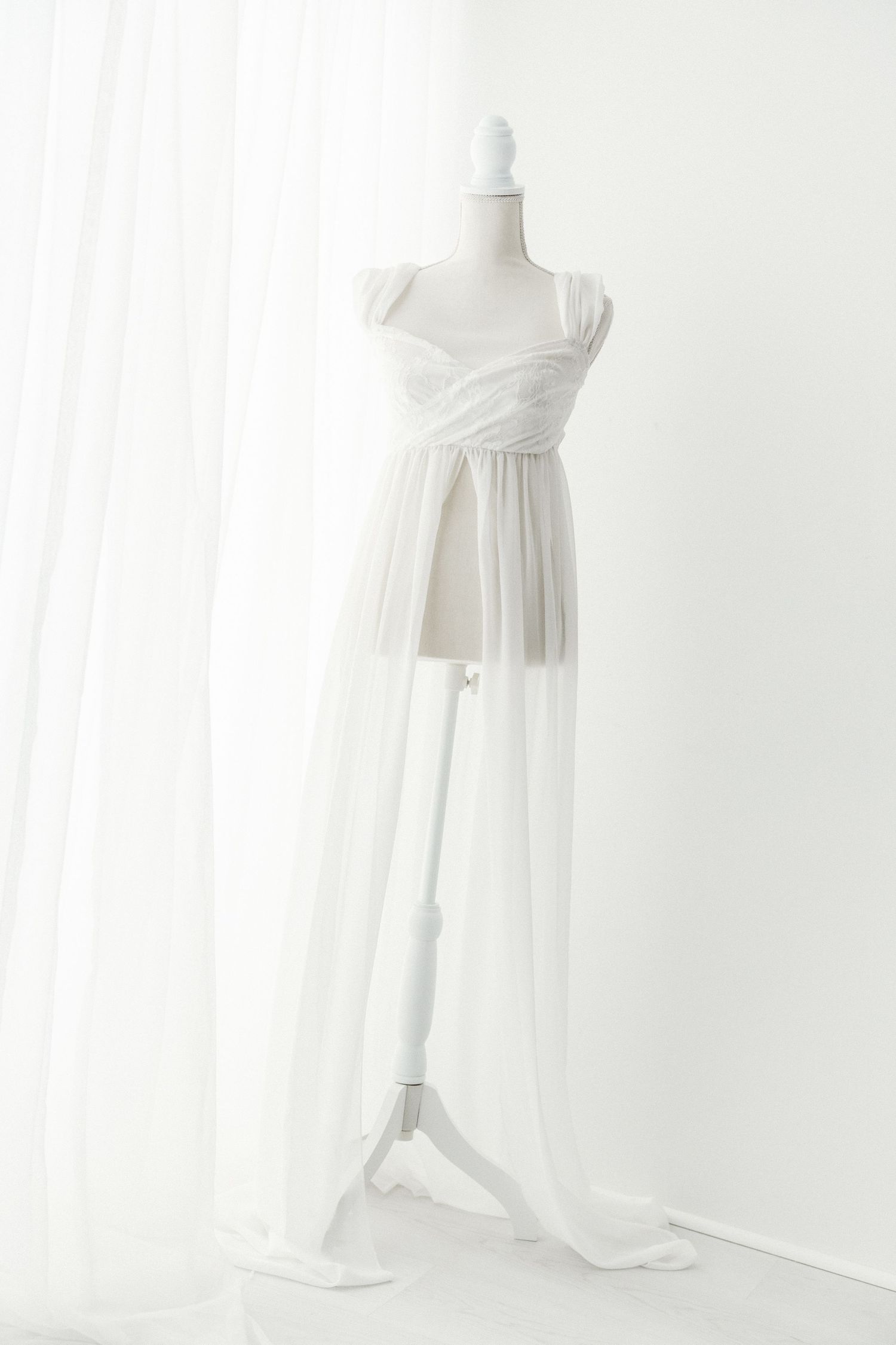 Elegant white tulle wrap gown with draped bodice and flowing skirt on a mannequin.