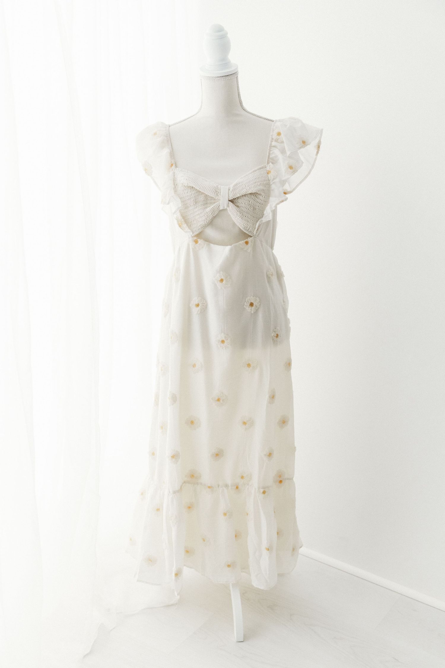 White floral embroidered maxi dress with ruffle straps and bow detail on mannequin.