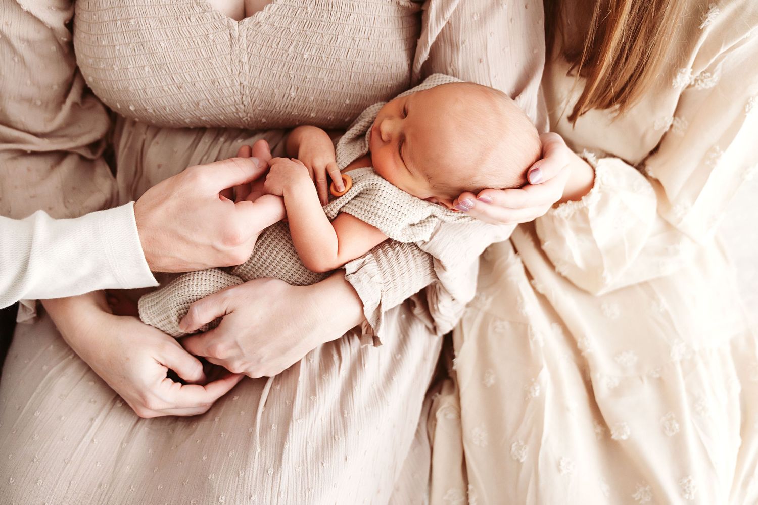 Parents hands cradling their sleeping newborn baby in soft neutral tones during a family session.