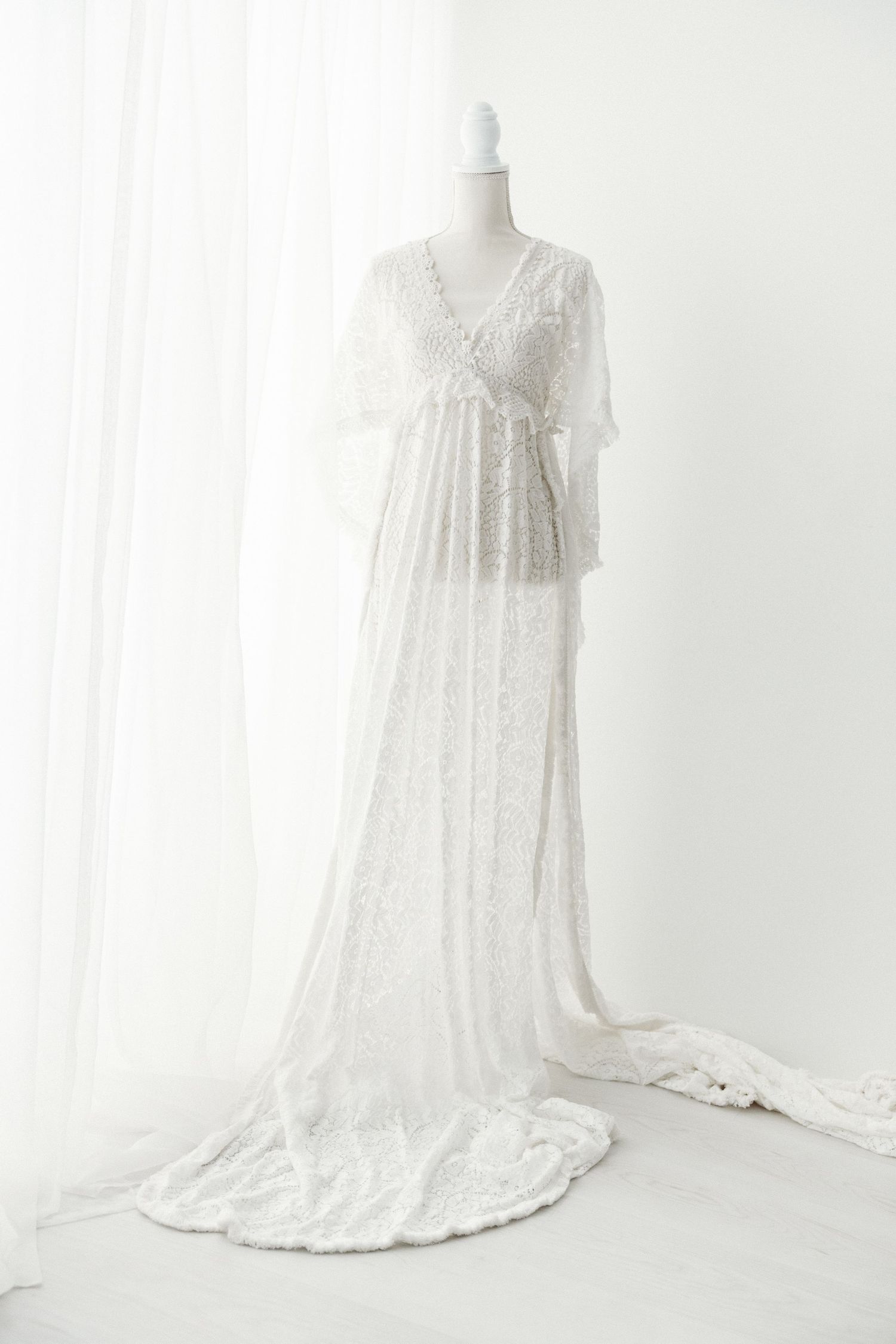 White lace flutter sleeve maternity gown with train on mannequin.