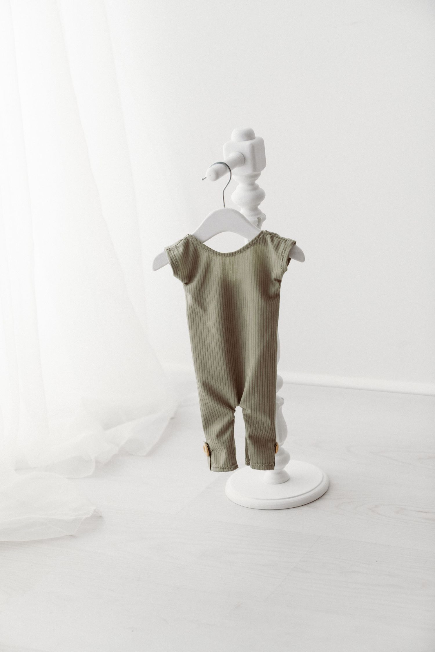 Olive green ribbed sleeveless baby romper displayed on a white decorative hanger stand against white background.