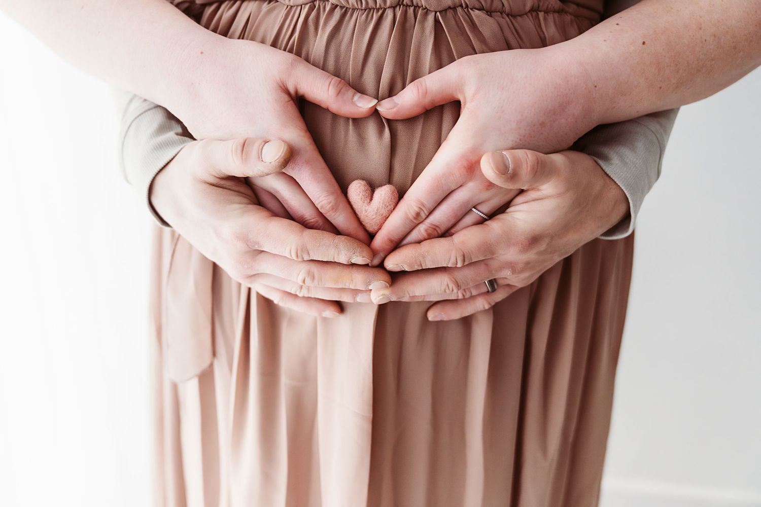 Two pairs of hands forming a heart shape on a pregnant woman's belly in a tender maternity photo.