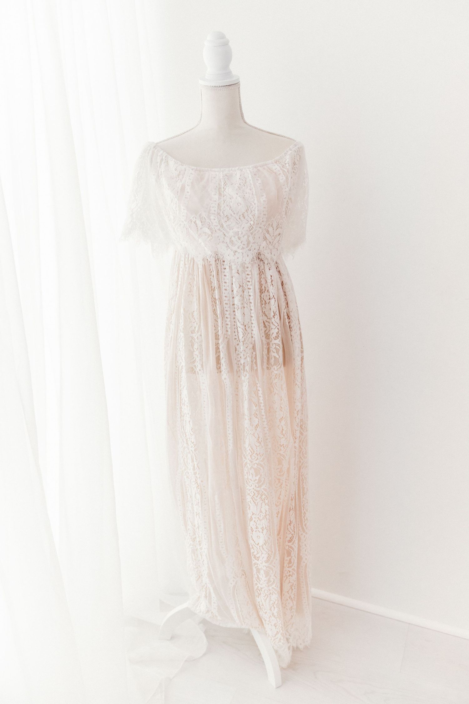 Blush off-shoulder lace maxi dress with feather trim and empire waist on a white mannequin.
