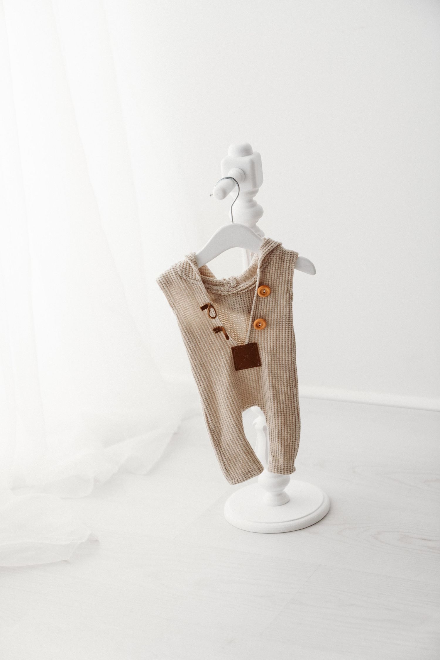 Beige ribbed baby overalls with brown buttons on a white decorative hanger stand against a white background.