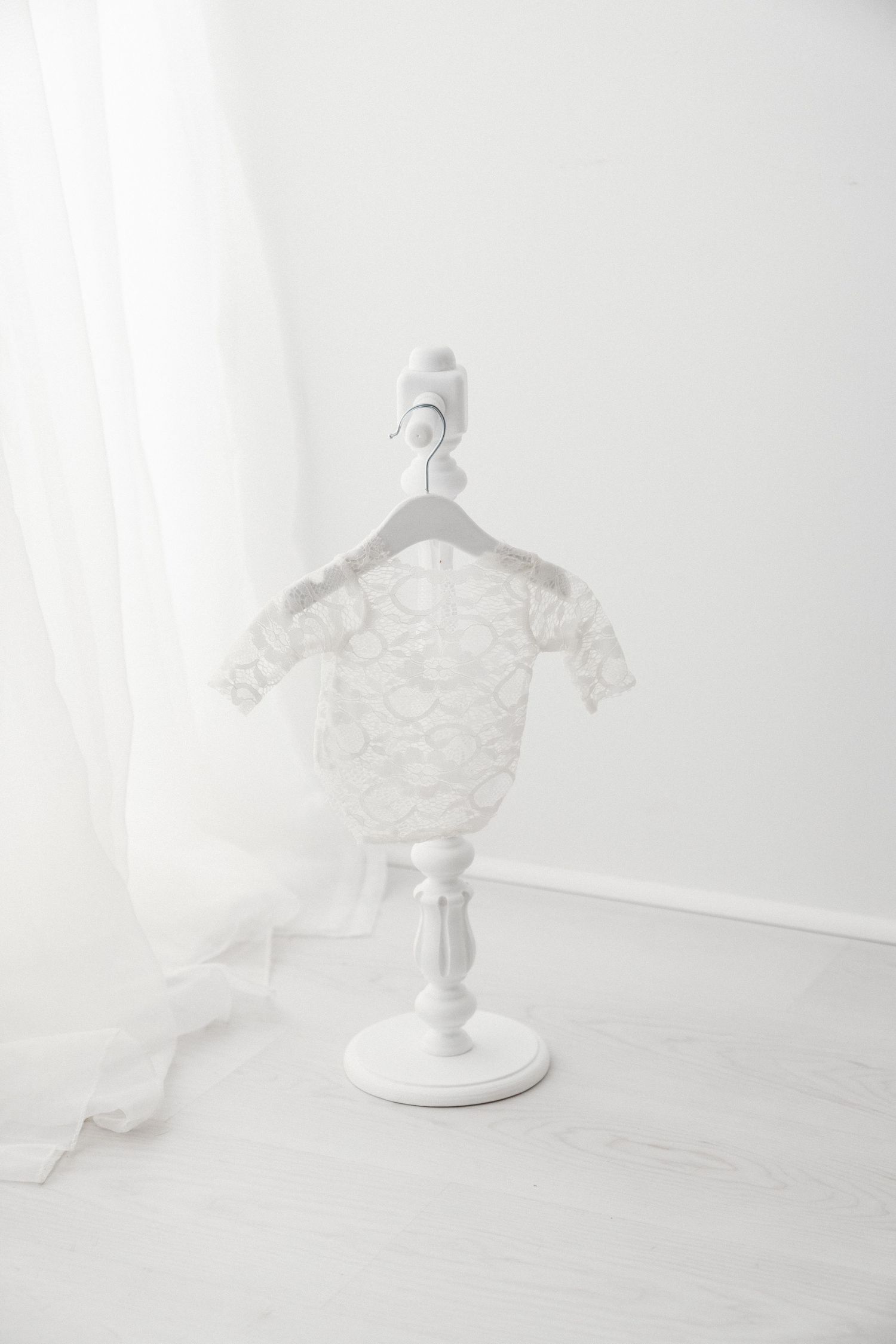 White lace long-sleeve baby romper with floral pattern displayed on a white decorative mini stand.