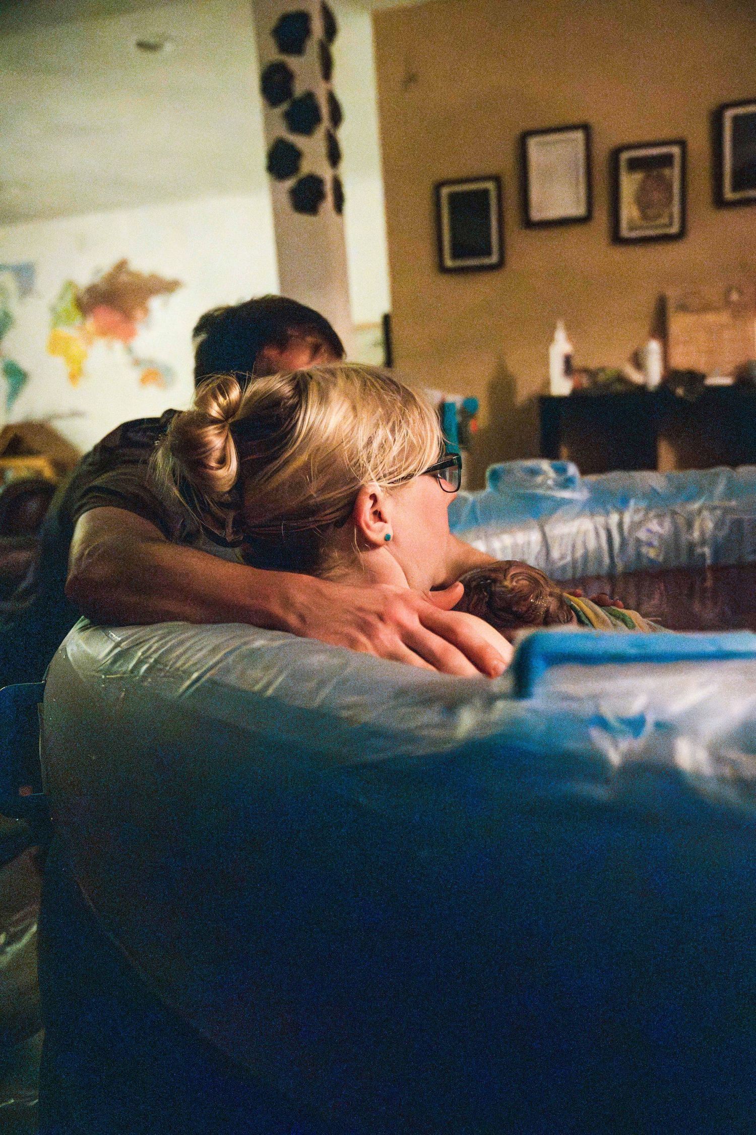 Woman leaning on inflatable birth pool during home water birth with partner providing support.