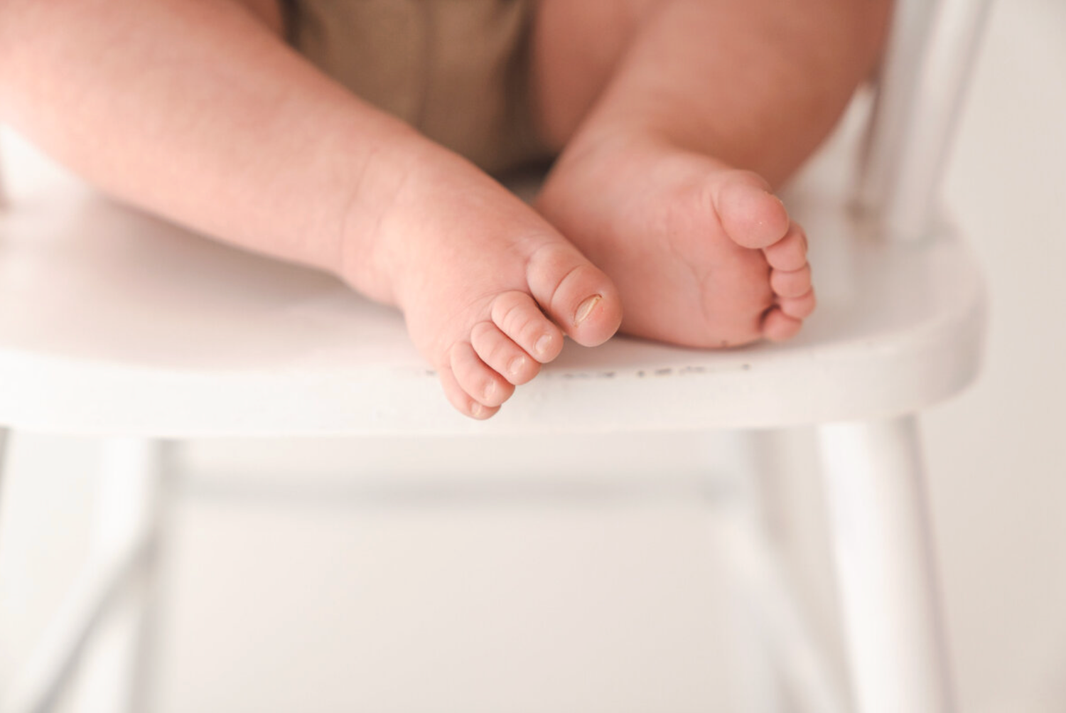 Close-up of tiny newborn baby feet resting on white high chair in studio photo.