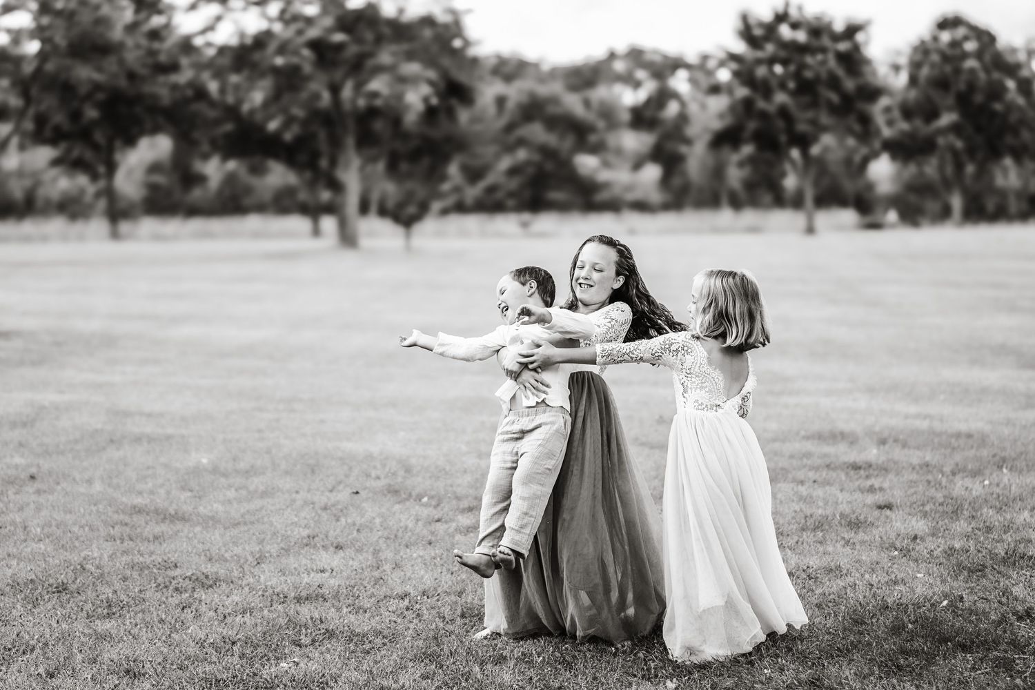 Black and white photo of mother spinning and playing with two children outdoors.