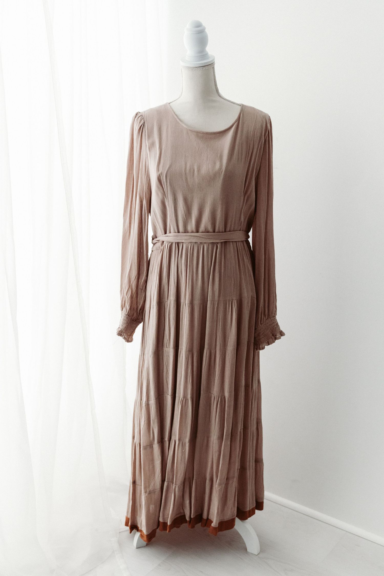 Taupe long sleeve belted pleated maxi dress with ruffle cuffs on mannequin.