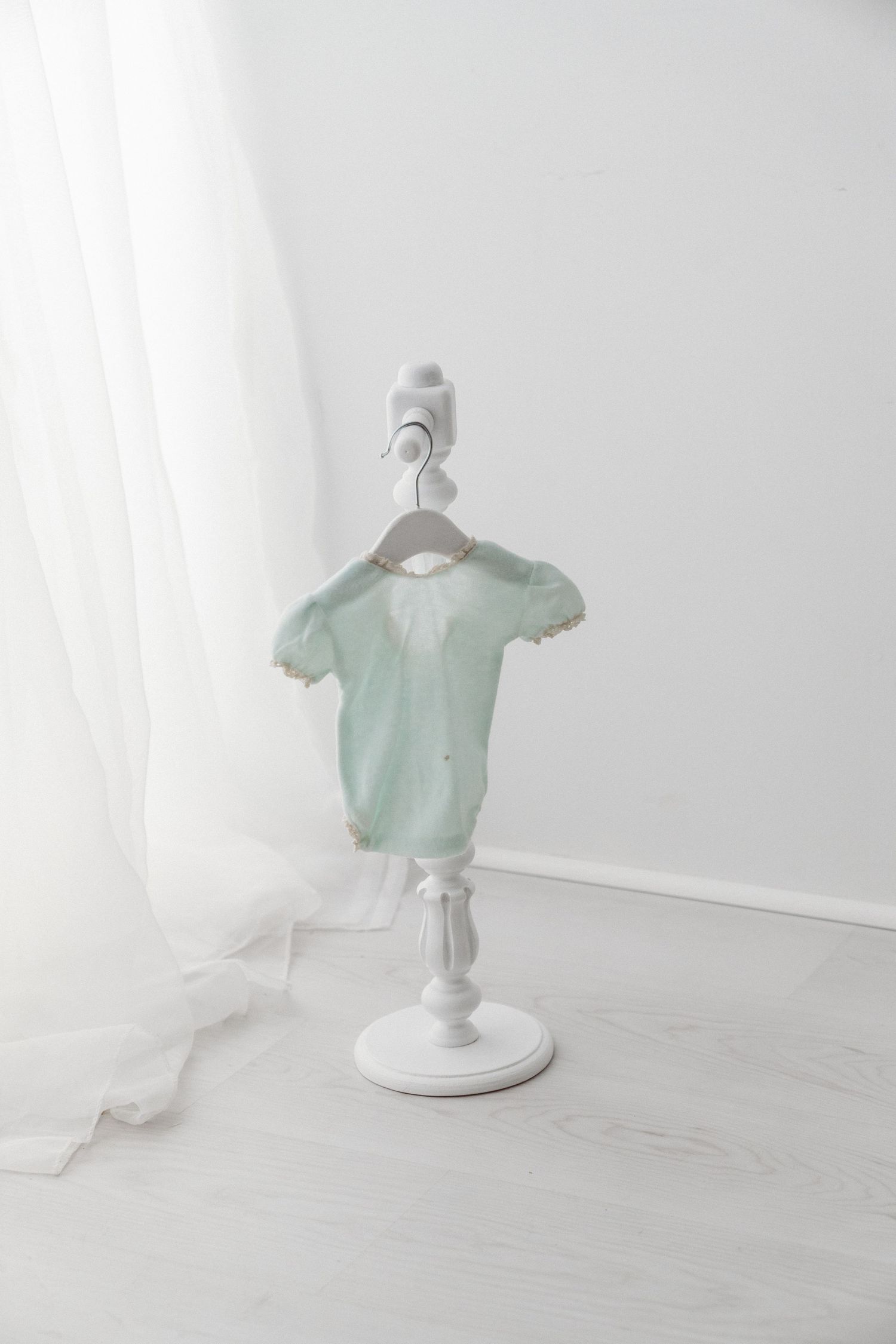 Mint green knit baby onesie with scalloped trim displayed on a white decorative mini stand.
