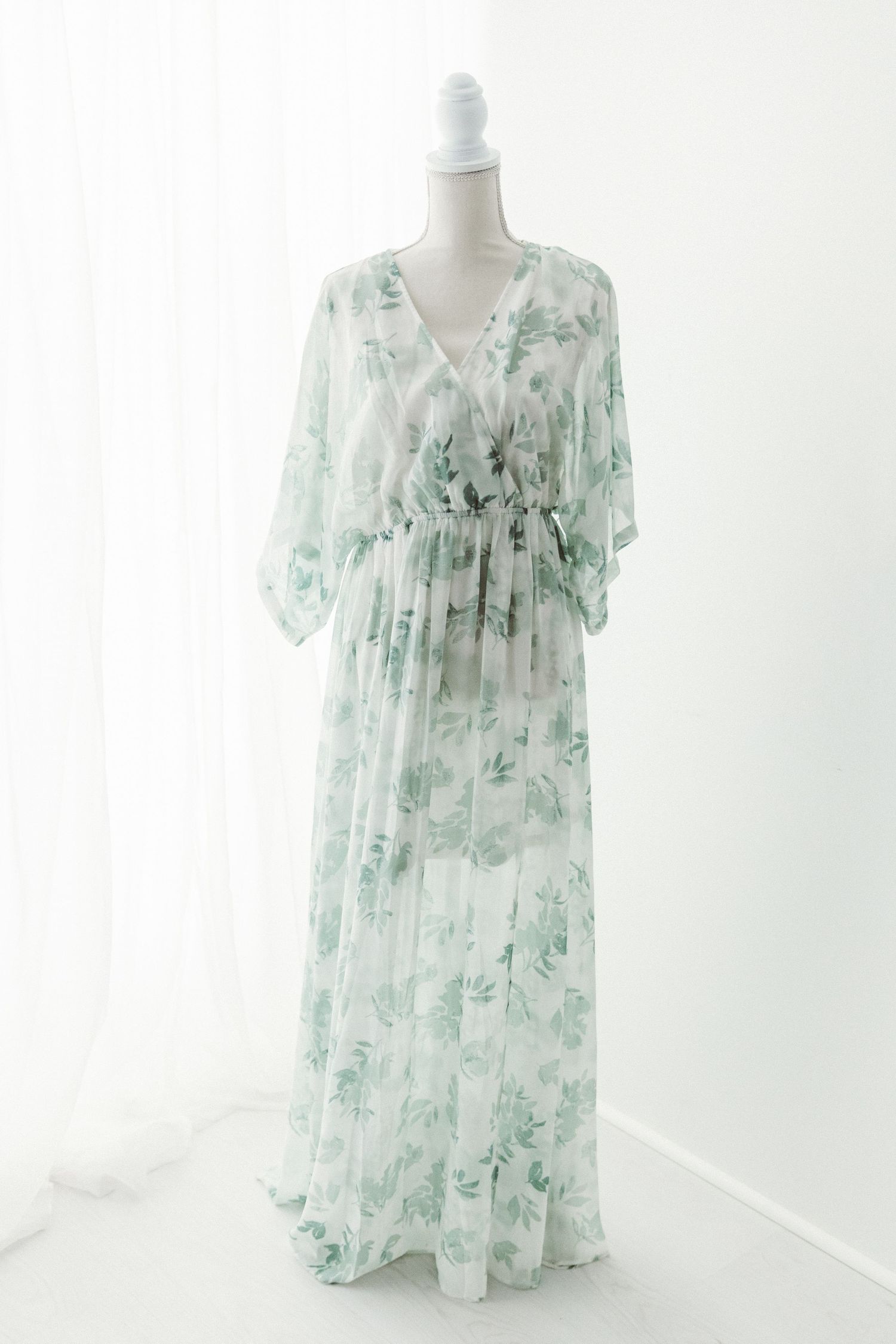 White chiffon maxi dress with green floral print, cinched waist, and flutter sleeves on a mannequin.