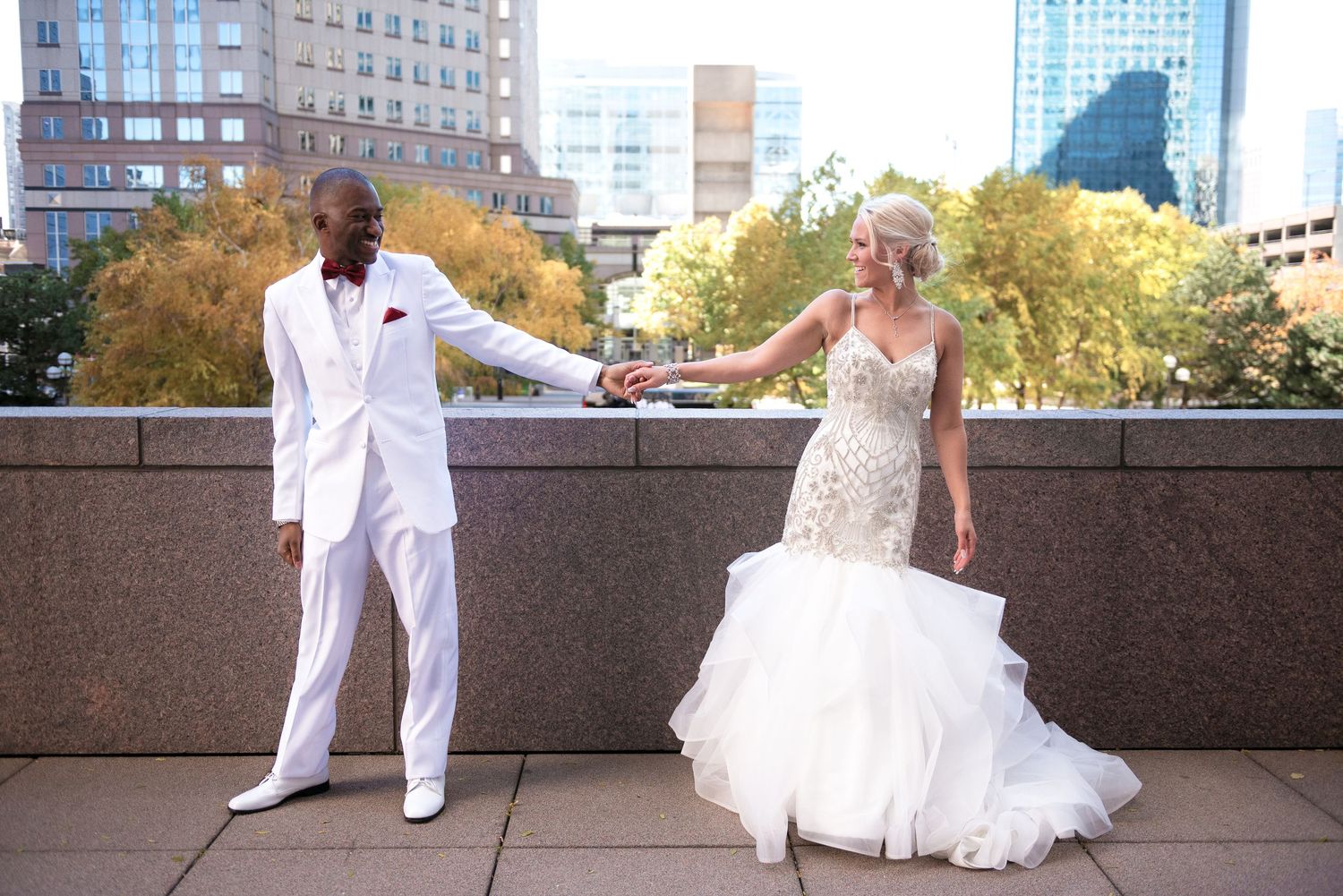 Elegant newlywed couple holding hands outdoors in a city setting in wedding attire.