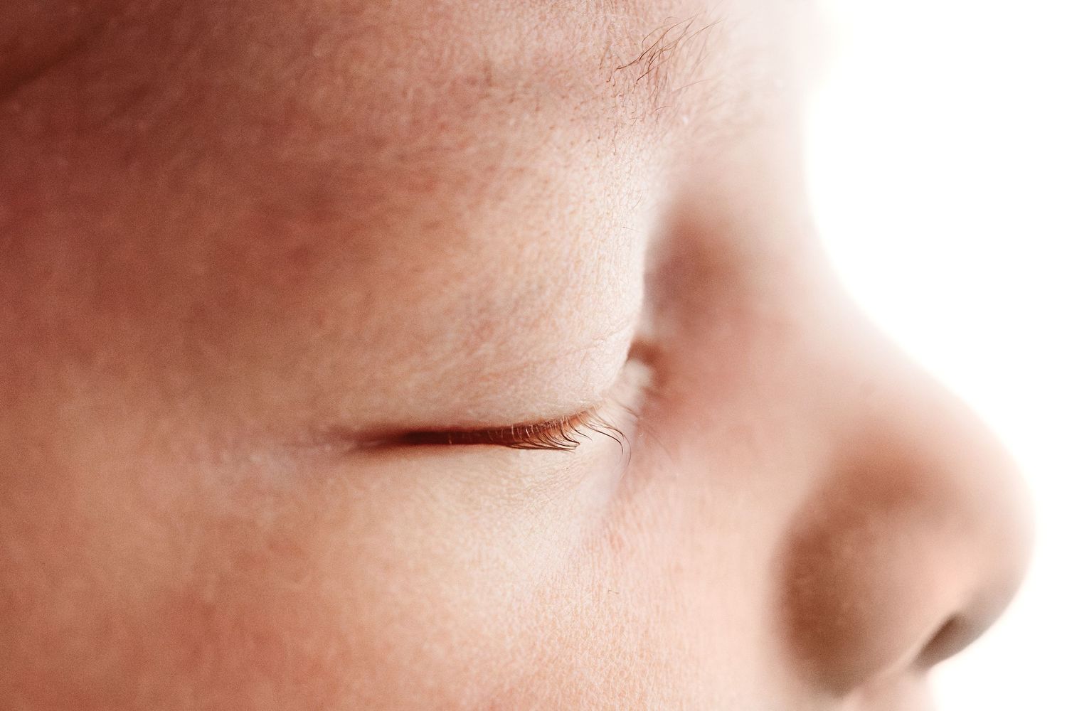 Close-up of a sleeping newborn baby's closed eye and nose on white background.