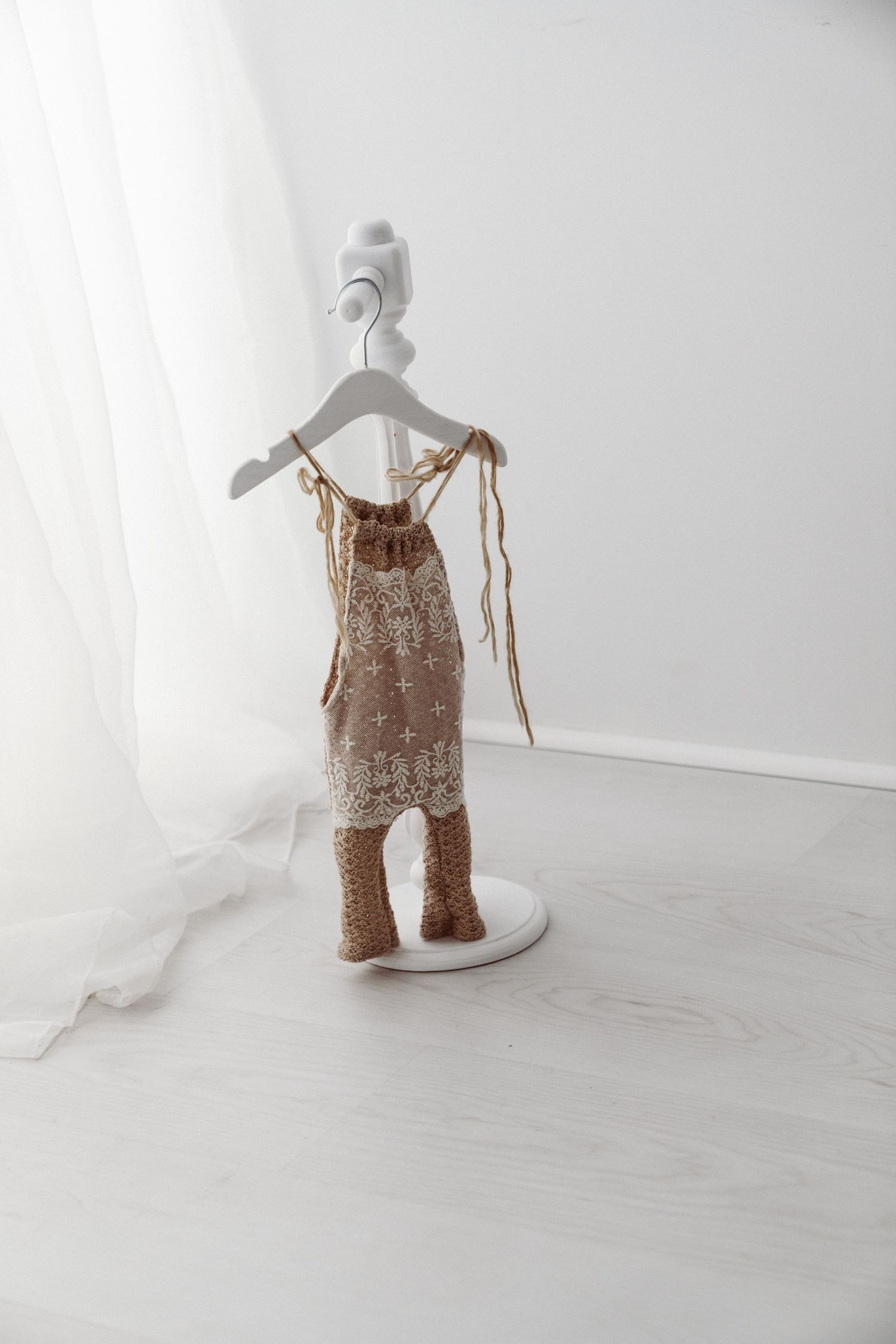 Brown knitted baby dress with lace overlay and matching booties on a white decorative mini hanger stand in white room.