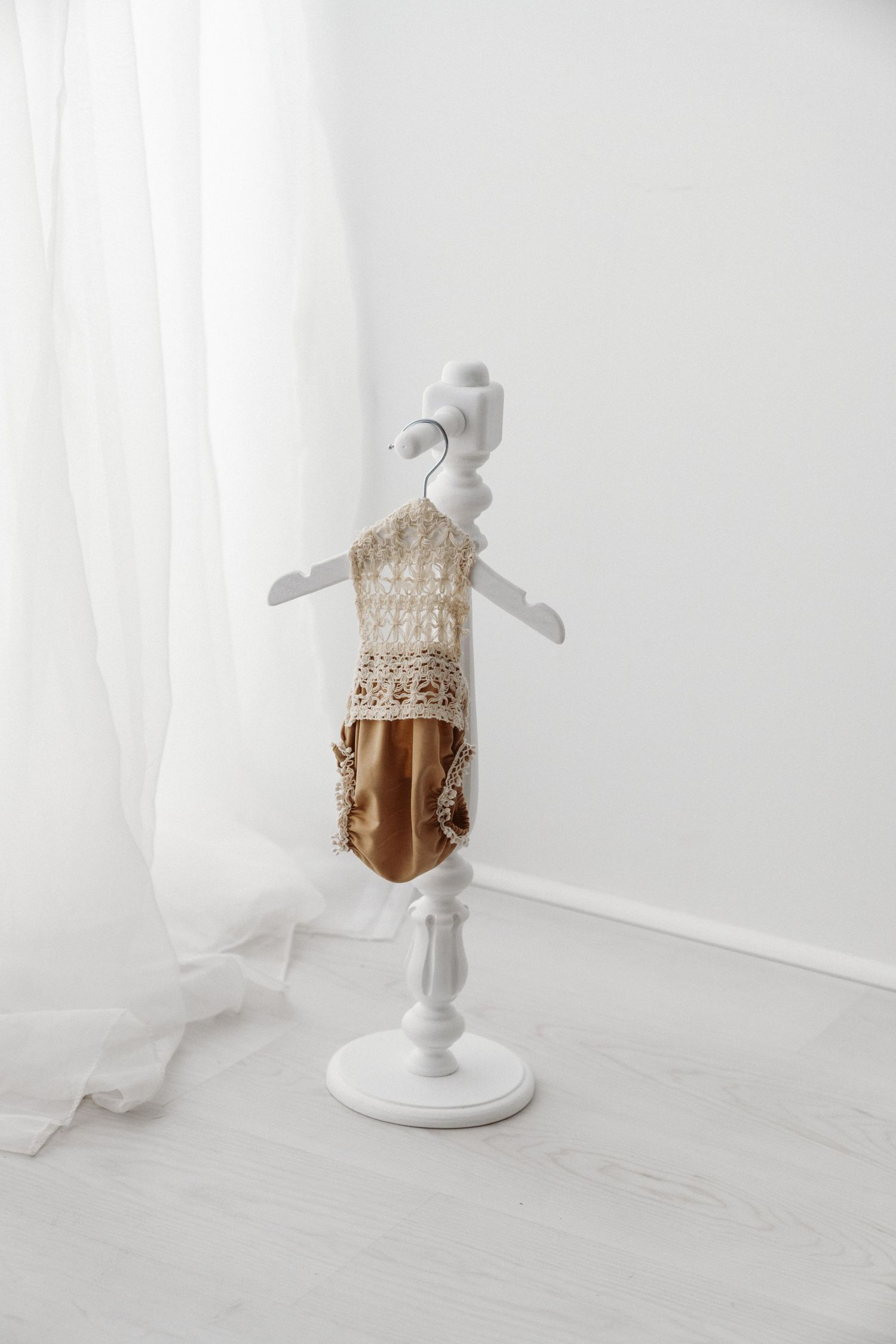 A delicate gold and lace newborn outfit displayed on a miniature white dress form stand.