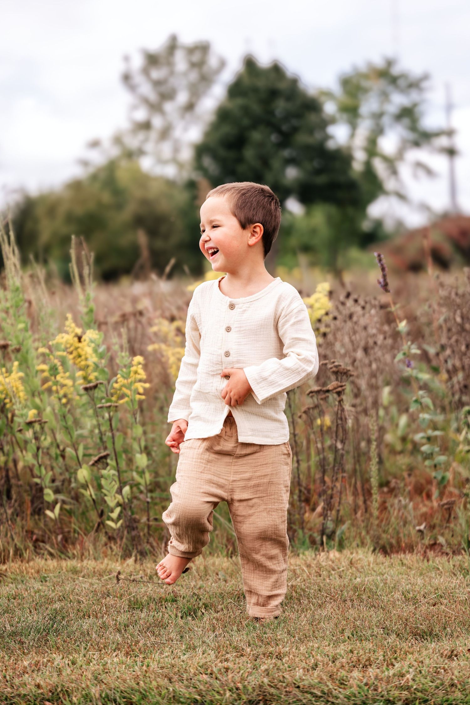 Happy toddler boy in cream shirt and tan pants runs through a meadow.