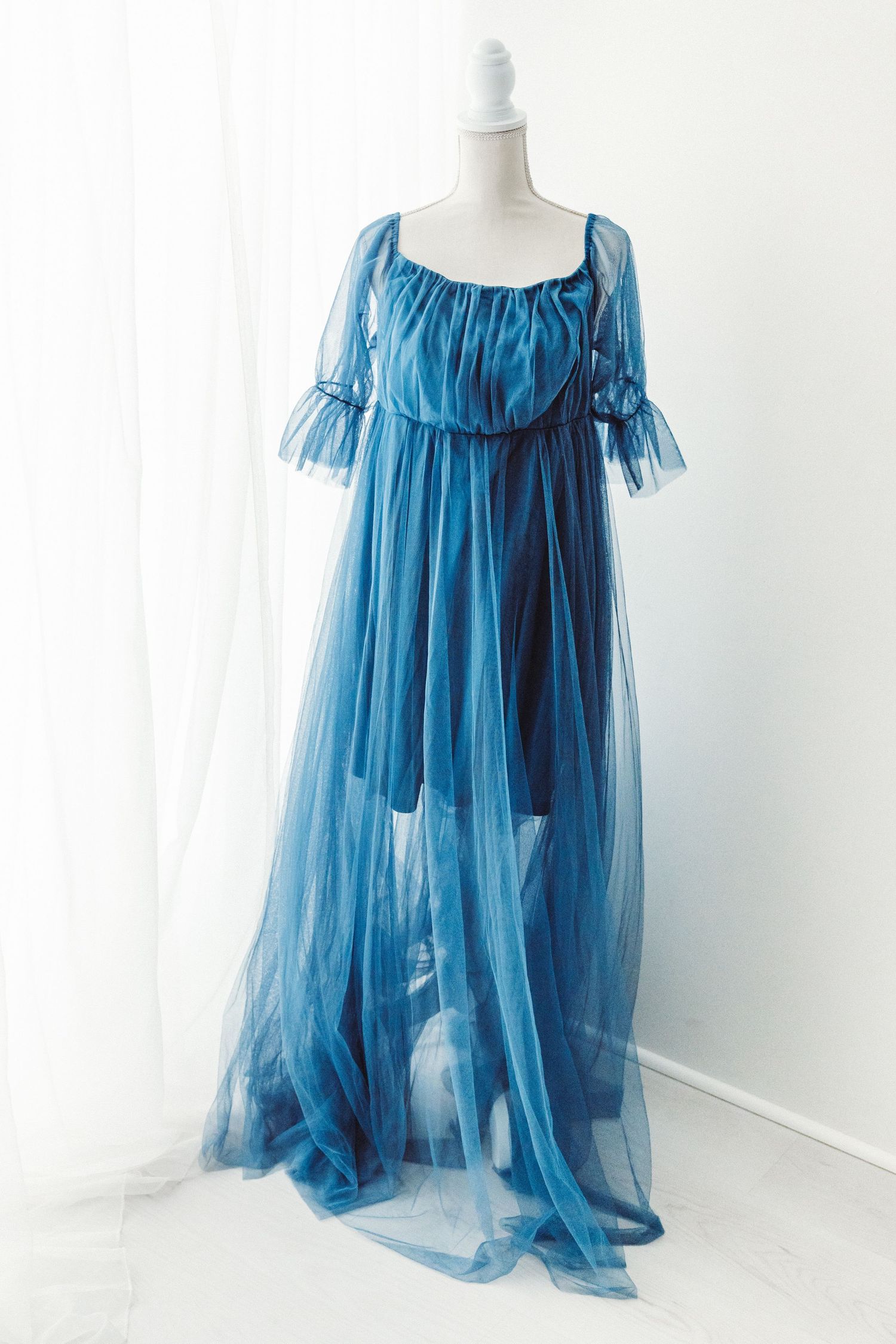 Sheer blue tulle off-shoulder maxi dress with ruffled neckline on a mannequin.