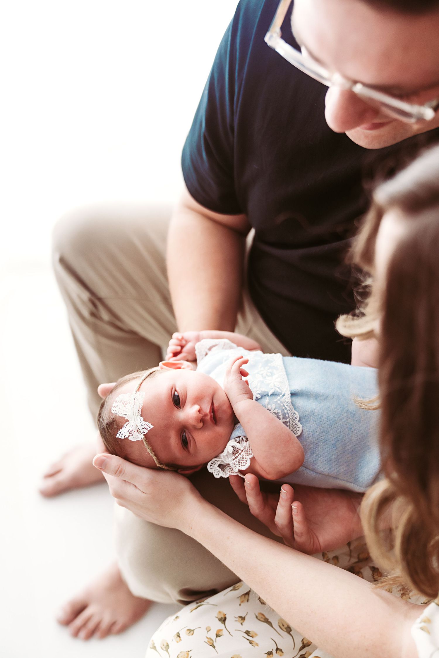 Parents holding their newborn baby girl wearing a blue outfit and floral headband indoors.