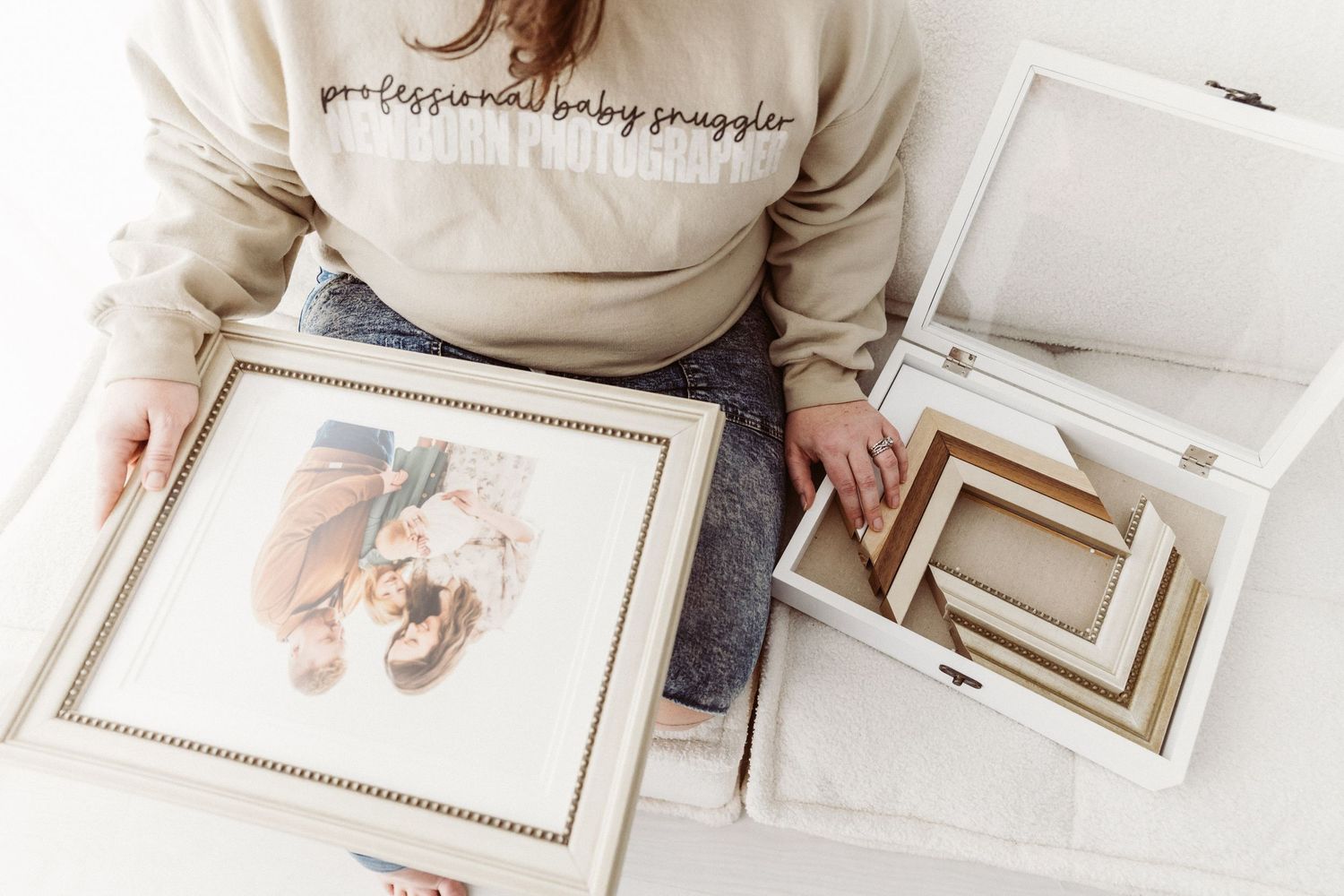 Woman in baby snuggler sweatshirt holding framed newborn photo with heirloom box.