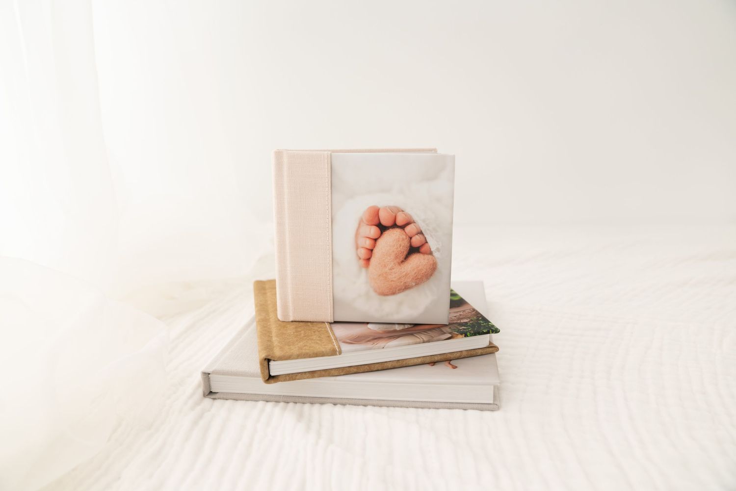 A newborn photo album with a baby foot cover image stacked on books on a white bed.