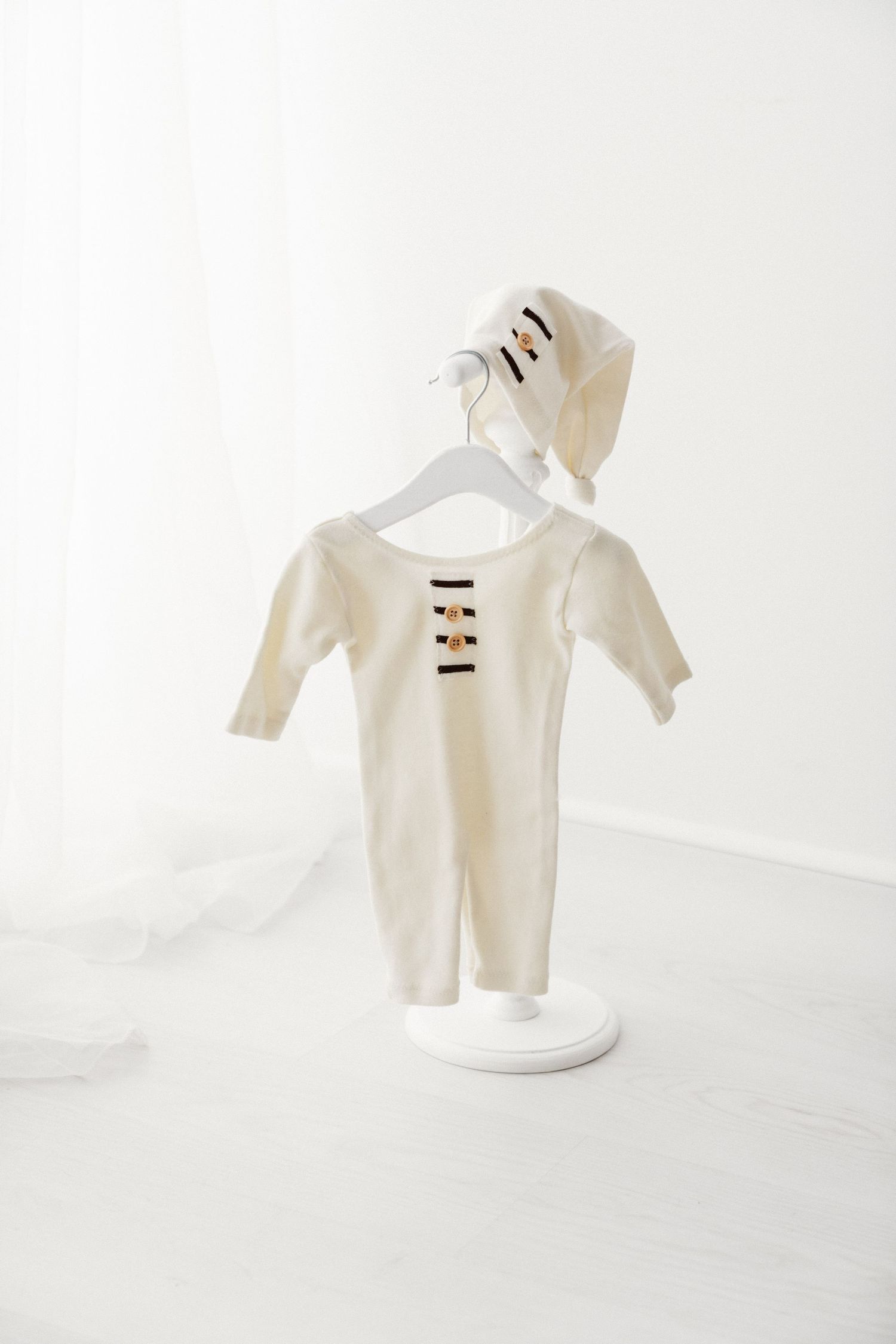 Cream knit baby romper with striped detail and matching bonnet hat on a white hanger stand.