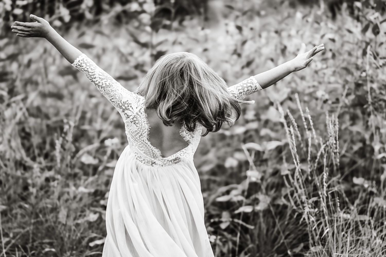 Black and white photo of woman in lace wedding dress with arms outstretched in nature.