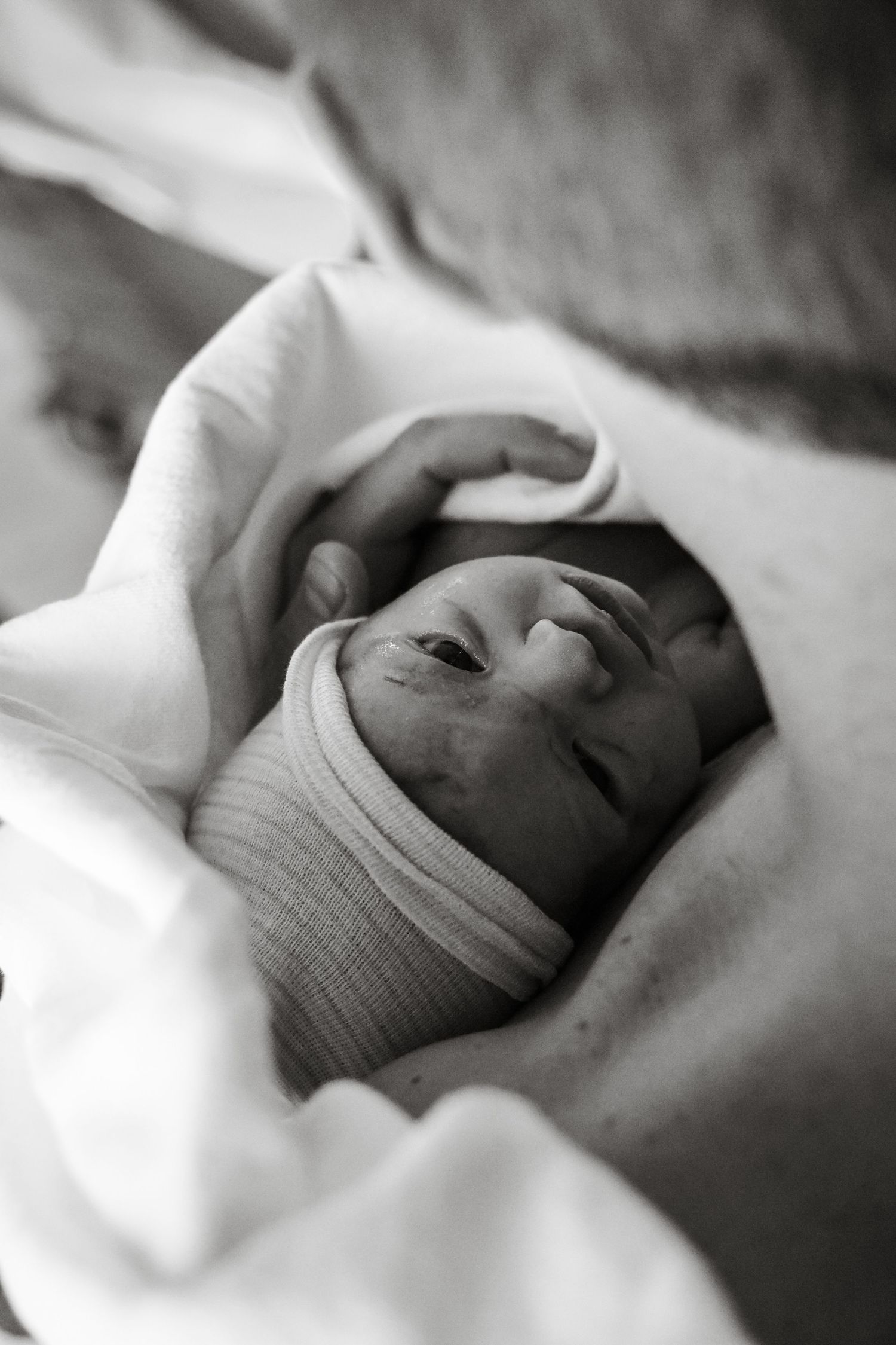 Black and white portrait of a swaddled newborn baby with eyes open in hospital nursery.