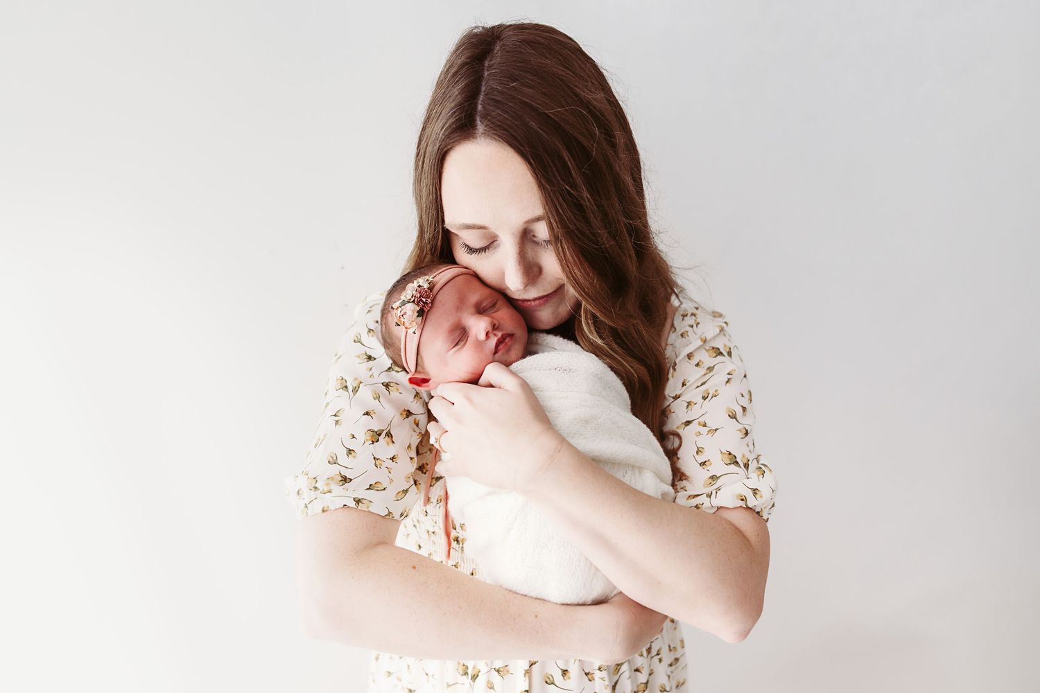 Young mother in floral dress tenderly holding her sleeping newborn baby close.
