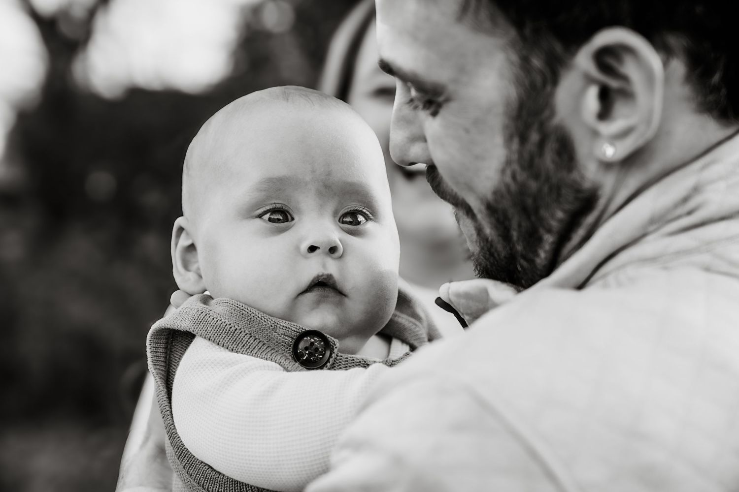 Black and white close-up of a bearded father holding his wide-eyed infant baby outdoors.