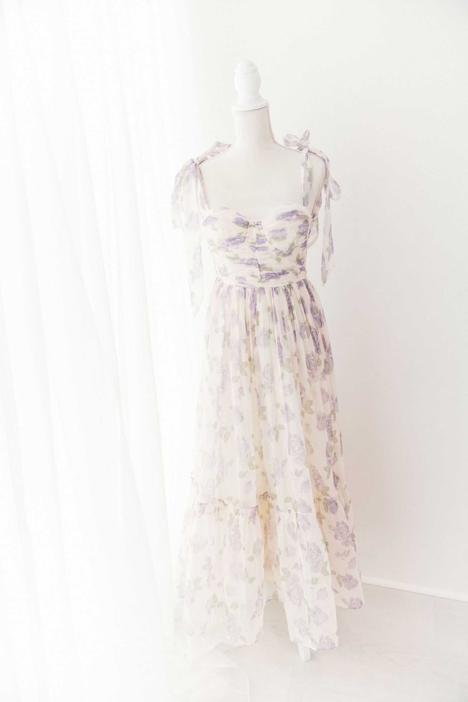 Ivory floral chiffon maxi dress with purple roses and tie shoulders displayed on a mannequin.
