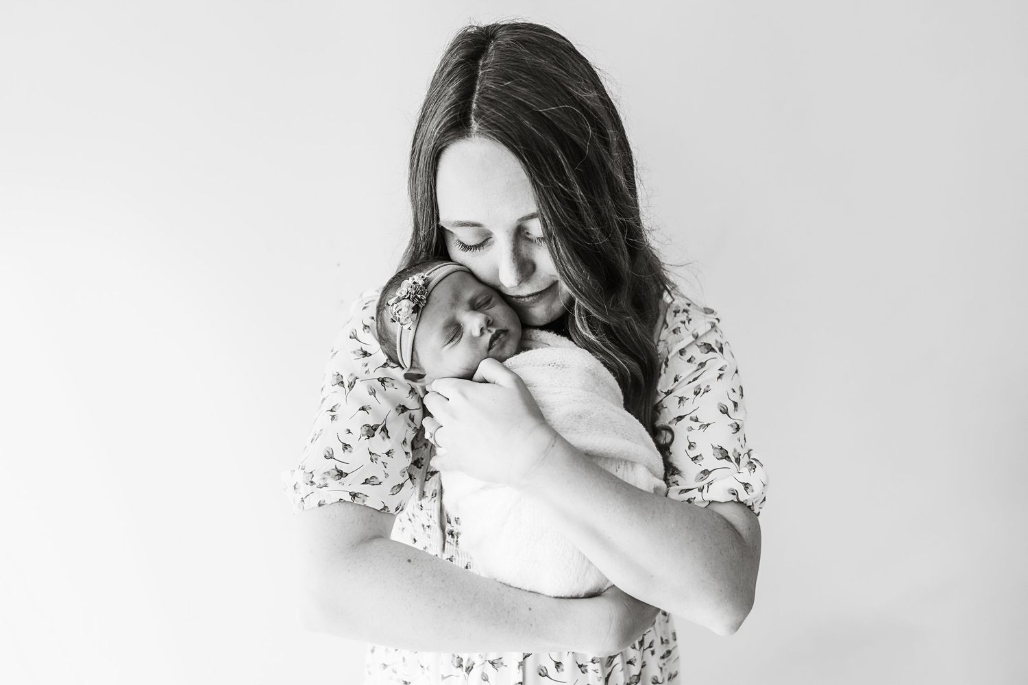 A black and white photo of a mother gently cradling and gazing at her swaddled newborn baby closely.