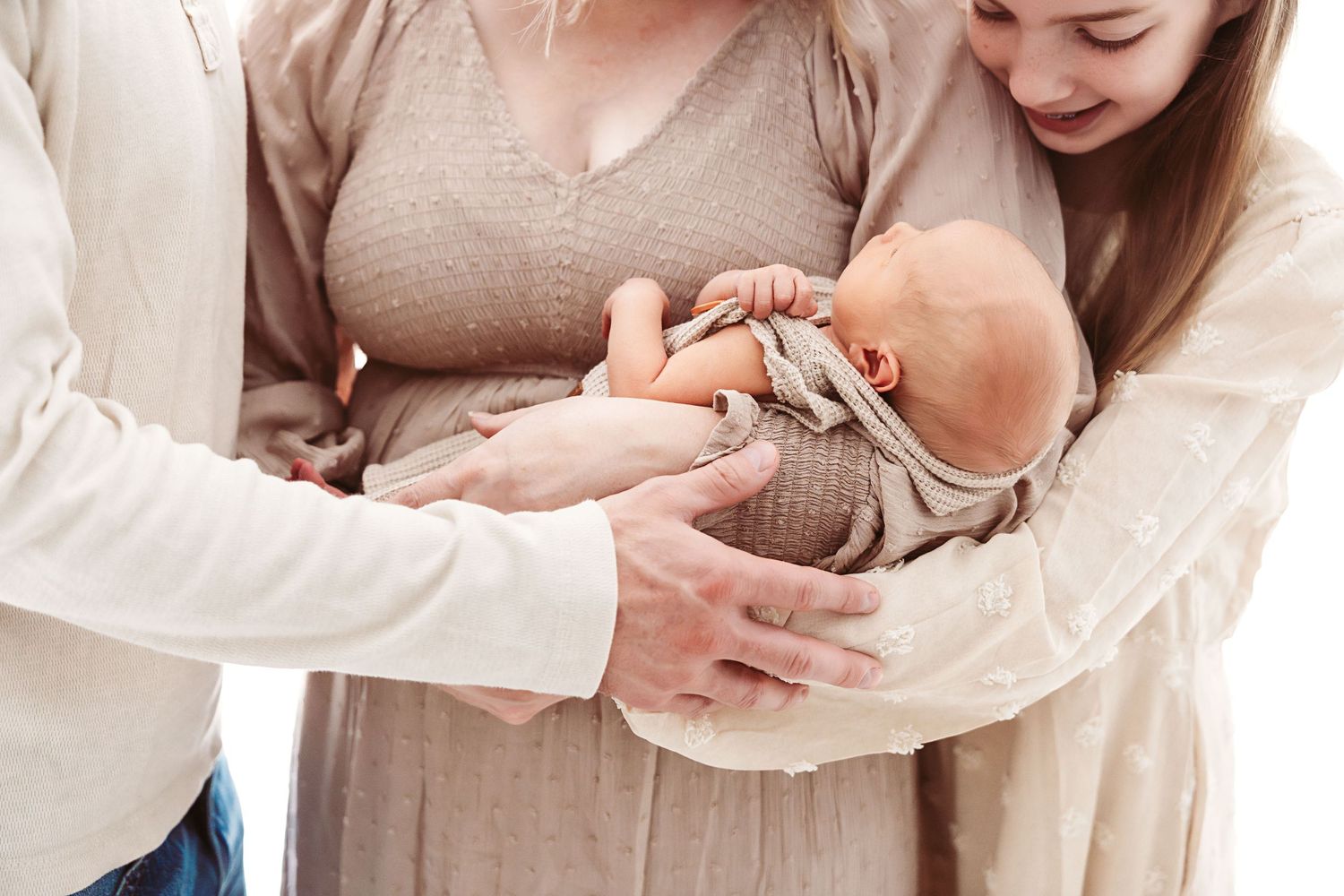 Family with newborn baby, parents and sibling gently holding infant in soft neutral tones.