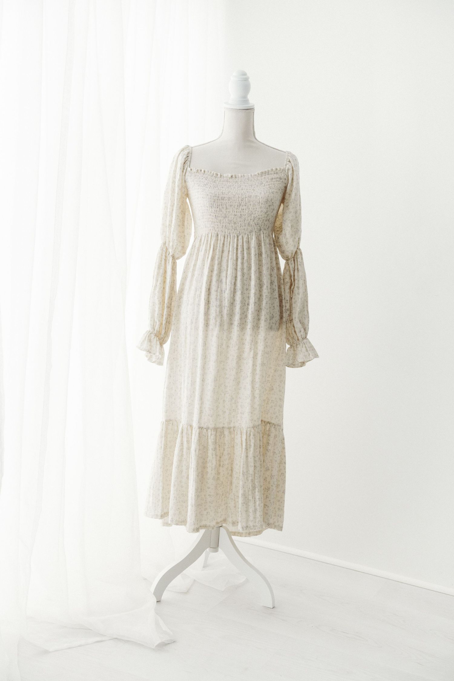 Cream floral long sleeve midi dress with smocked bodice and tiered skirt on mannequin.